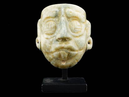 ANCIENT PRE COLUMBIAN MAYAN CARVED GREEN JADE MASK: An ancient Mesoamerican Pre Columbian Mayan carved green jade mask. The mask depicts a stylized human face with distinct features such as prominent eyes with geometric design, a prominent nose, and a