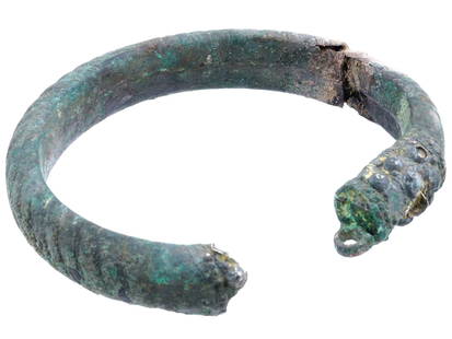 ANCIENT ROMAN BRONZE BRACELET WITH OPEN DESIGN: An ancient Roman bronze bracelet, a relic of classical antiquity. The torc is circular with an open design, crafted from a thick piece of metal showing green patina. One end of the torc features a rai