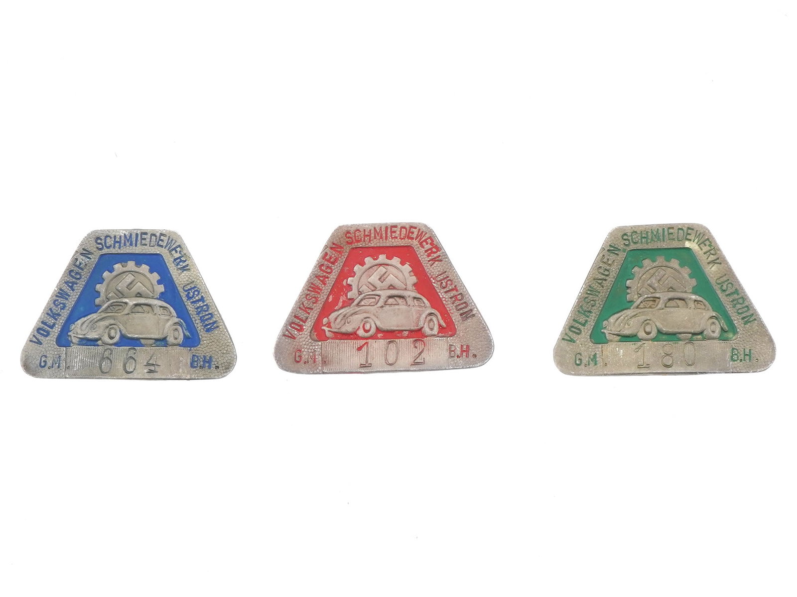 GROUP OF THREE GERMAN WWII TYPE VOLKSWAGEN EMPLOYEE BADGES: A group of three WWII model Nazi German Third Reich Volkswagen factory employee shields. The badges are covered with enamel in red, blue and green shades, featuring an image of a car with a swastika i