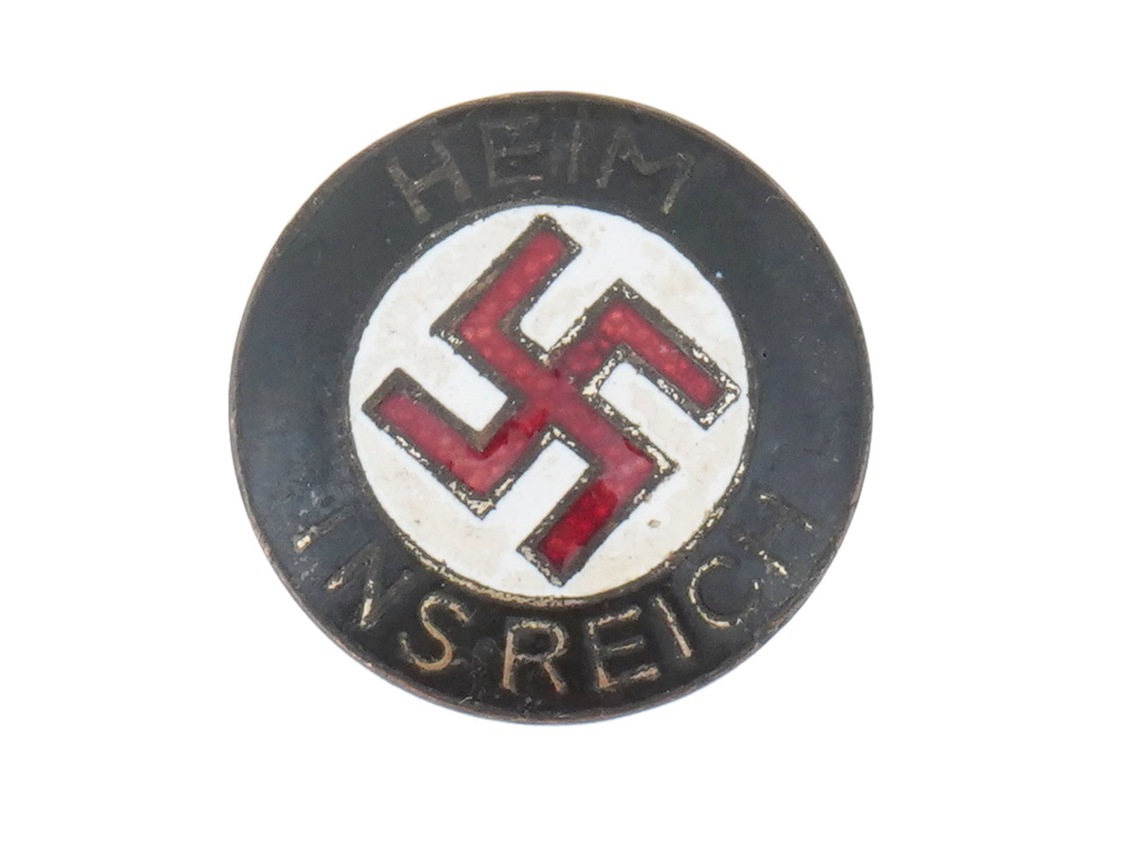WWII NAZI GERMAN NSDAP IN LUXEMBOURG ENAMEL BADGE: A WWII National Socialist German Workers Party enamel pin badge featuring a red enamel swastika in the center with the inscription Heim Ins Reich, Home to the Reich. Refers to the badges of the German