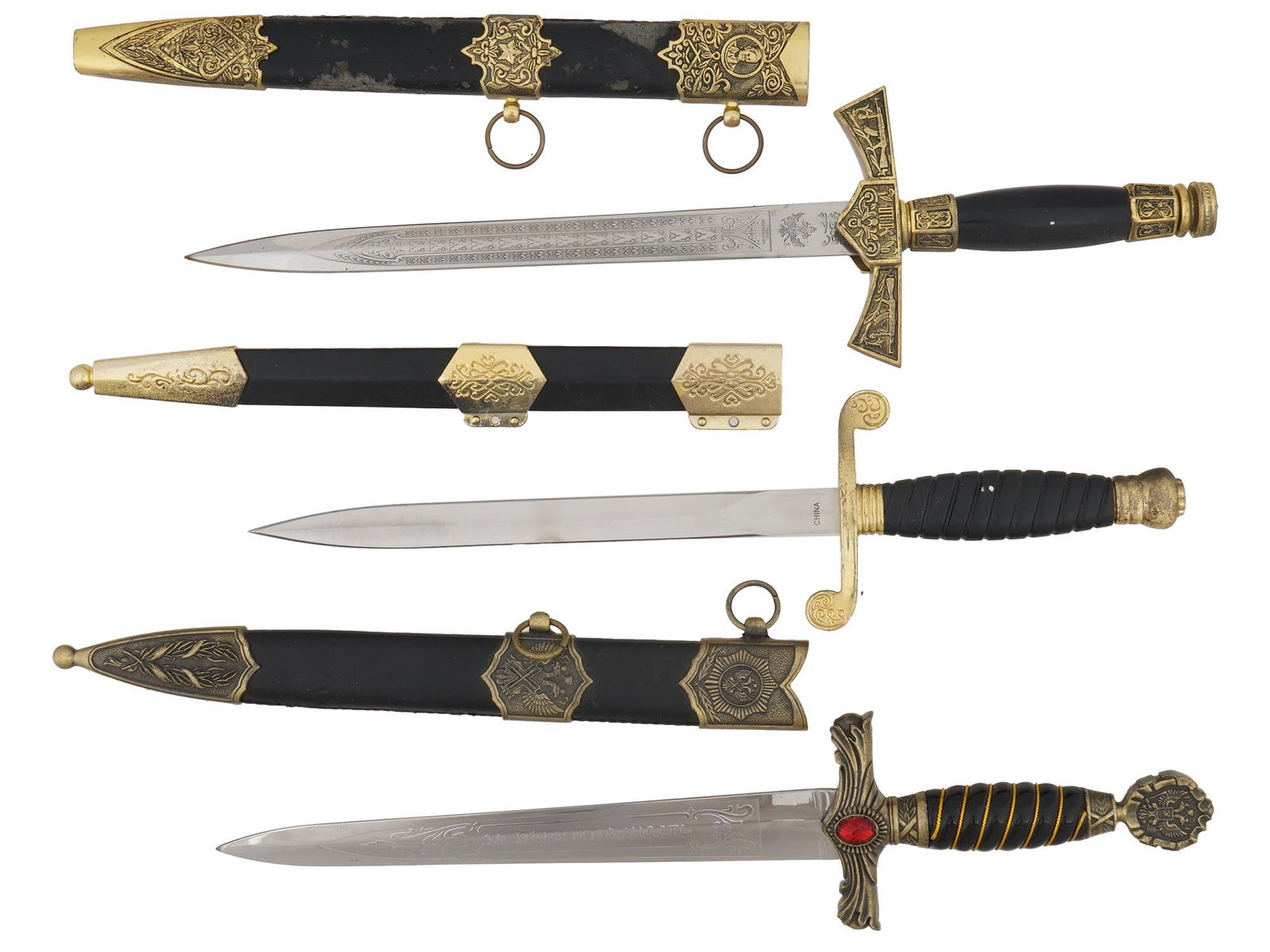 GROUP OF THREE RUSSIAN MILITARY DAGGERS WITH SCABBARDS: A group of three Russian daggers. The first features a stainless steel double-edged blade with full floral engravings, a glossy black handle, and a brass crossguard engraved with the letters and an im