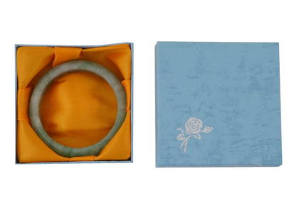 CHINESE HAND CARVED JADE BANGLE BRACELET IN BOX: A Chinese hand carved Nephrite Jade bangle bracelet in white and green shades. Circa: the first half of the 20th century. Jade bracelet is considered a symbol of parental love and protection. Presente