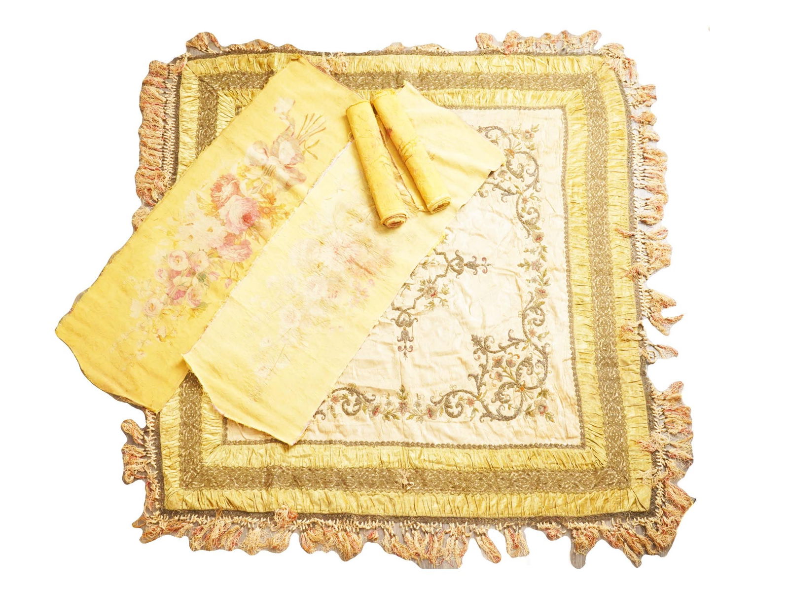 ASSORTMENT OF DECORATIVE FABRIC COVERS W FLORAL DESIGN: An assortment of decorative fabric covers includes a square cover featuring intricate embroidered patterns featuring a floral motif. It is adorned with a fringe trim. A set of four rectangular covers,