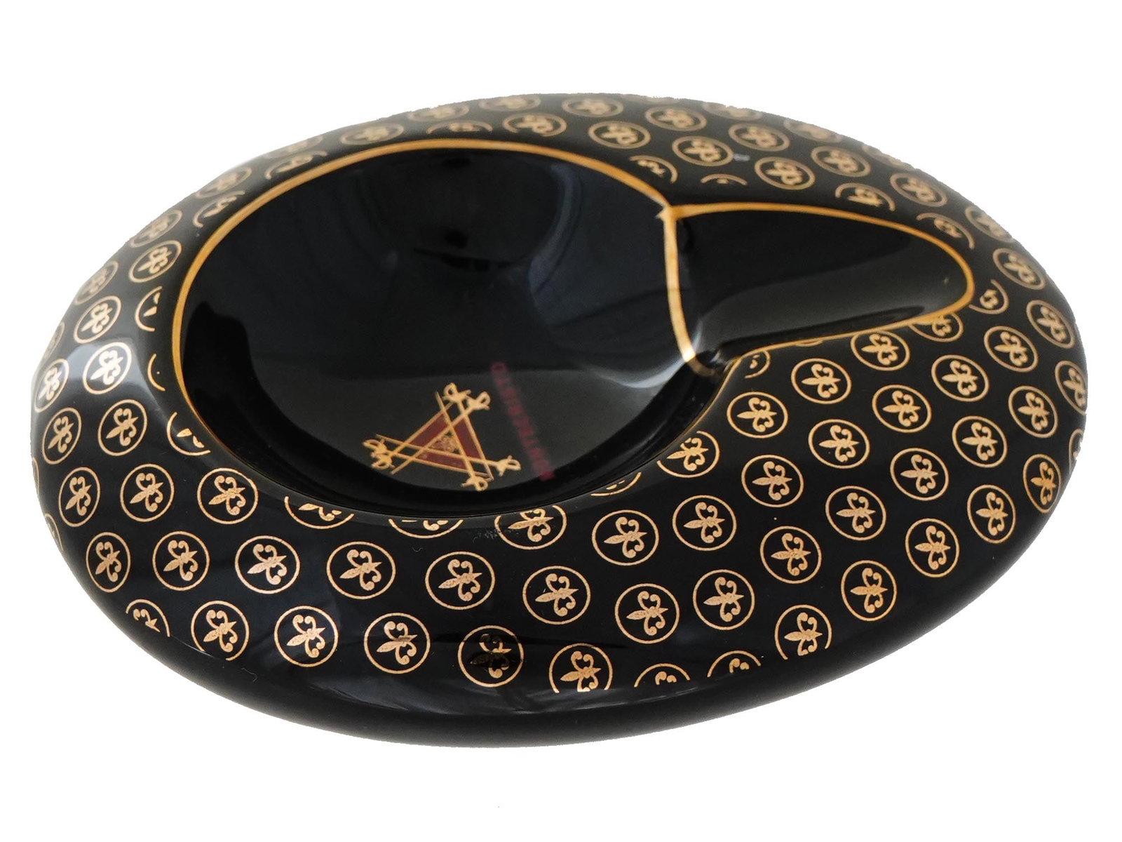 VINTAGE BLACK CIGAR ASHTRAY BY MONTECRISTO: A vintage black oval shaped single caliber cigar ashtray with gold clorored decor by Montecristo. The outer surface of the ashtray is covered in a repeating pattern of gold fleur de lis symbols, each 