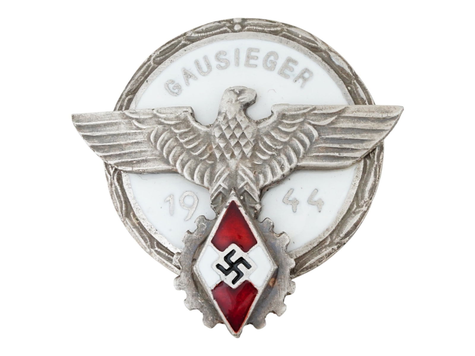 WWII NAZI GERMAN HITLER YOUTH GAUSIEGER 1944 BADGE: A WWII Nazi German Hitler Youth enamel badge, Gausieger 1944, awarded to regional winners of National Socialist competitions, of circular form, featuring a border of oak leaves and an inscribed legend