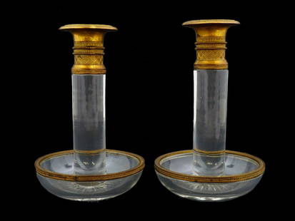 ANTIQUE EMPIRE GILT BRONZE CRYSTAL CANDLE HOLDERS: A pair of antique Empire candlesticks. European, ca. 1900. Clear crystal stem and bobeche base, gilt bronze rim and top part. Embossed acanthus leaf and twirl ornaments. Unmarked. Collectible Glasswar