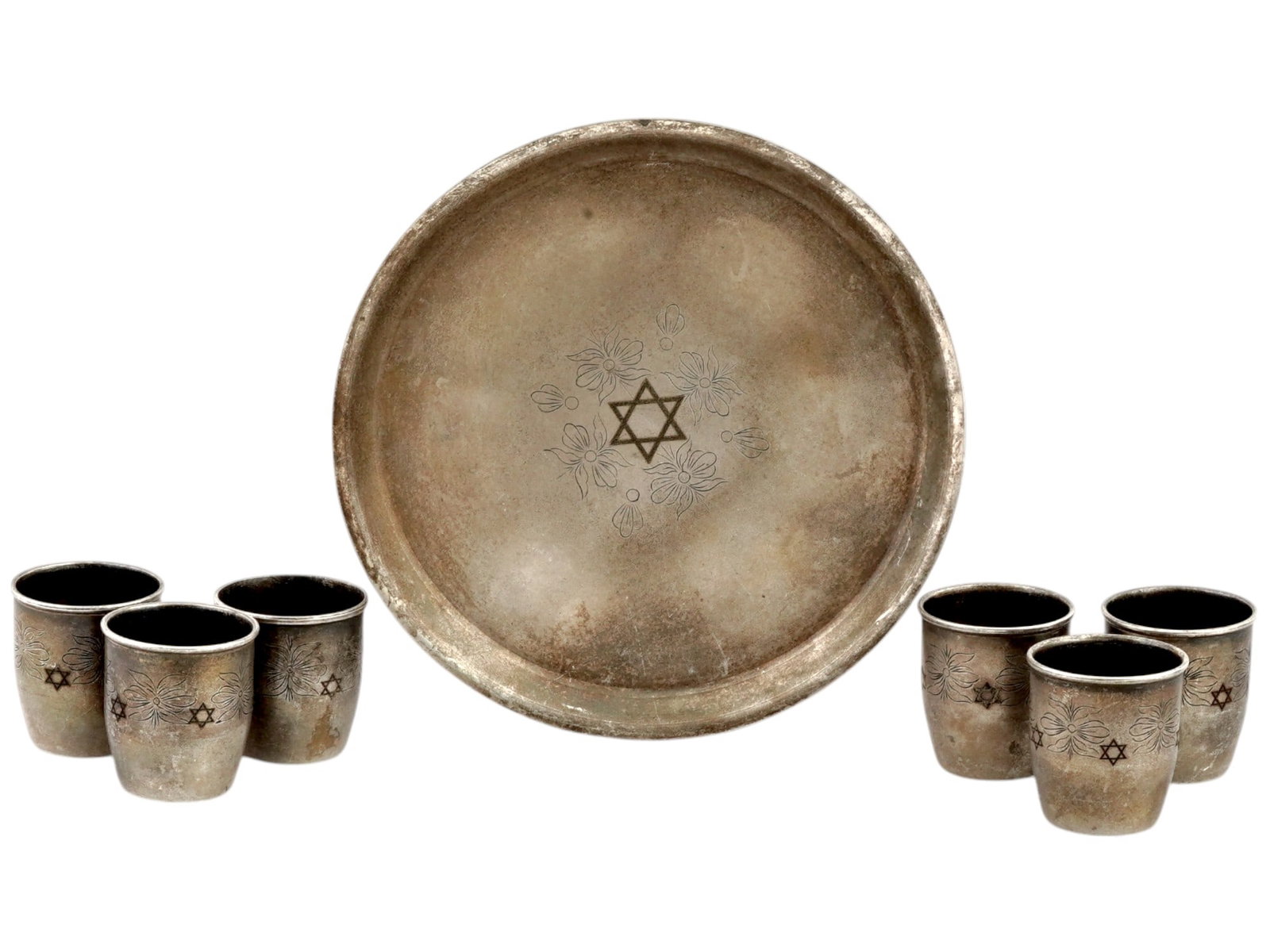POLISH JUDAICA KIDDUSH CUPS AND SERVING PLATE: An early to mid-20th century Polish brass shabbat tableware set. A total of 7 items, including 6 kiddush cups and a serving plate. Etched floral pattern and Magen David motif. Magen David with lion ha