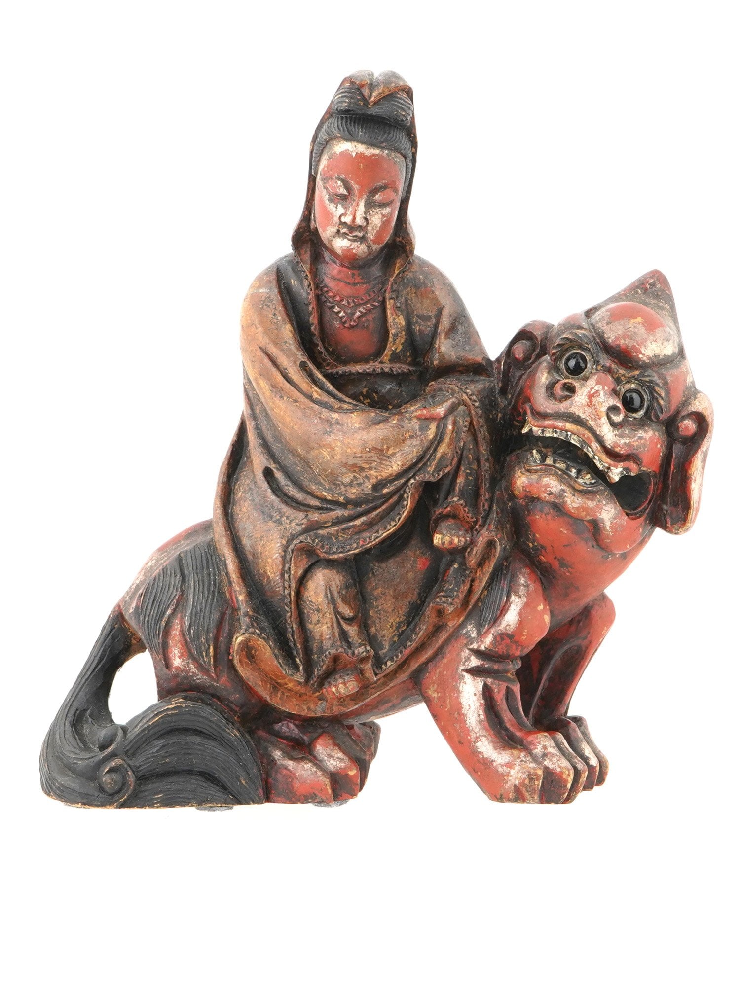 CHINESE WOODEN FIGURINE OF GUANYIN RIDING A FOO DOG: A Chinese hand carved wooden figurine of Guanyin riding a Foo Dog. The figurine is painted in red, black and gold. The figure of Guanyin sits atop the Foo Dog, who is depicted with a fierce expression