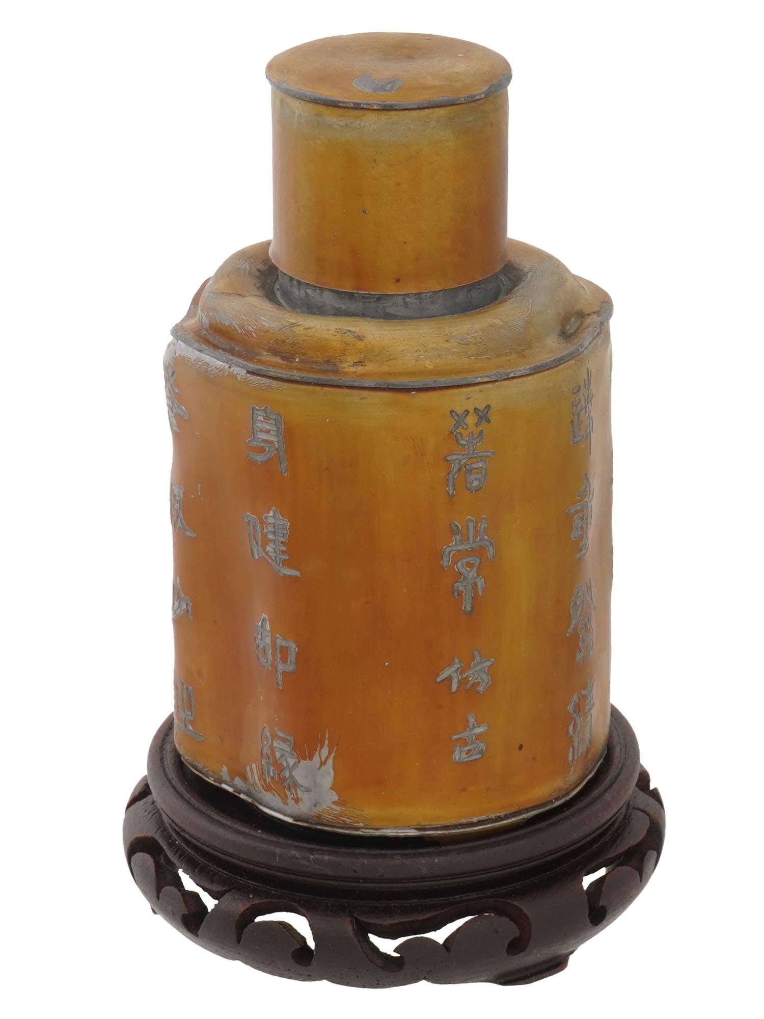 ANTIQUE CHINESE SWATOW PEWTER TEA CANISTER ON A BASE: An antique Chinese Swatow pewter tea canister, presented on a carved wooden base. This cylindrical container features traditional form and subtle decorative detailing, characteristic of Swatow pewter