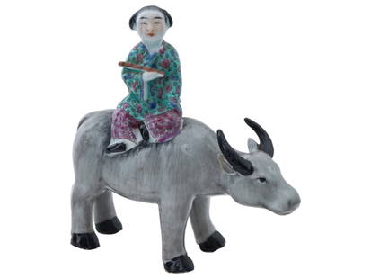CHINESE PORCELAIN FIGURINE HERDBOY RIDING BUFFALO: A vintage Chinese porcelain figurine depicting a herdboy riding a water buffalo. The boy is depicted with a traditional Chinese childrens hairstyle, holding a flute in his hand, and wearing green and