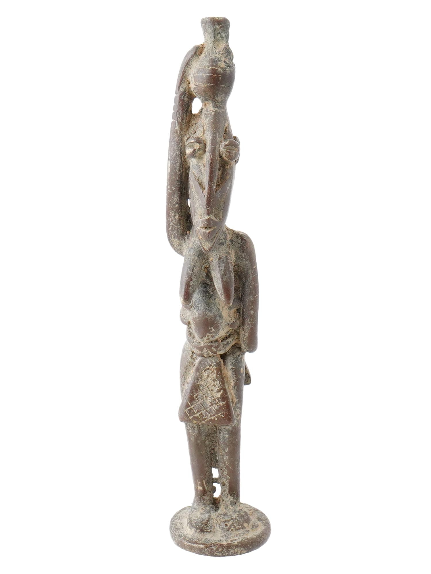 ANTIQUE DOGON BRONZE NUDE FEMALE FIGURE 1800 AD: An antique Dogon bronze nude female figure, circa the 1800 AD. The figure is depicted standing, with elongated limbs and stylized features, holding a child on her back and balancing a vessel on her he
