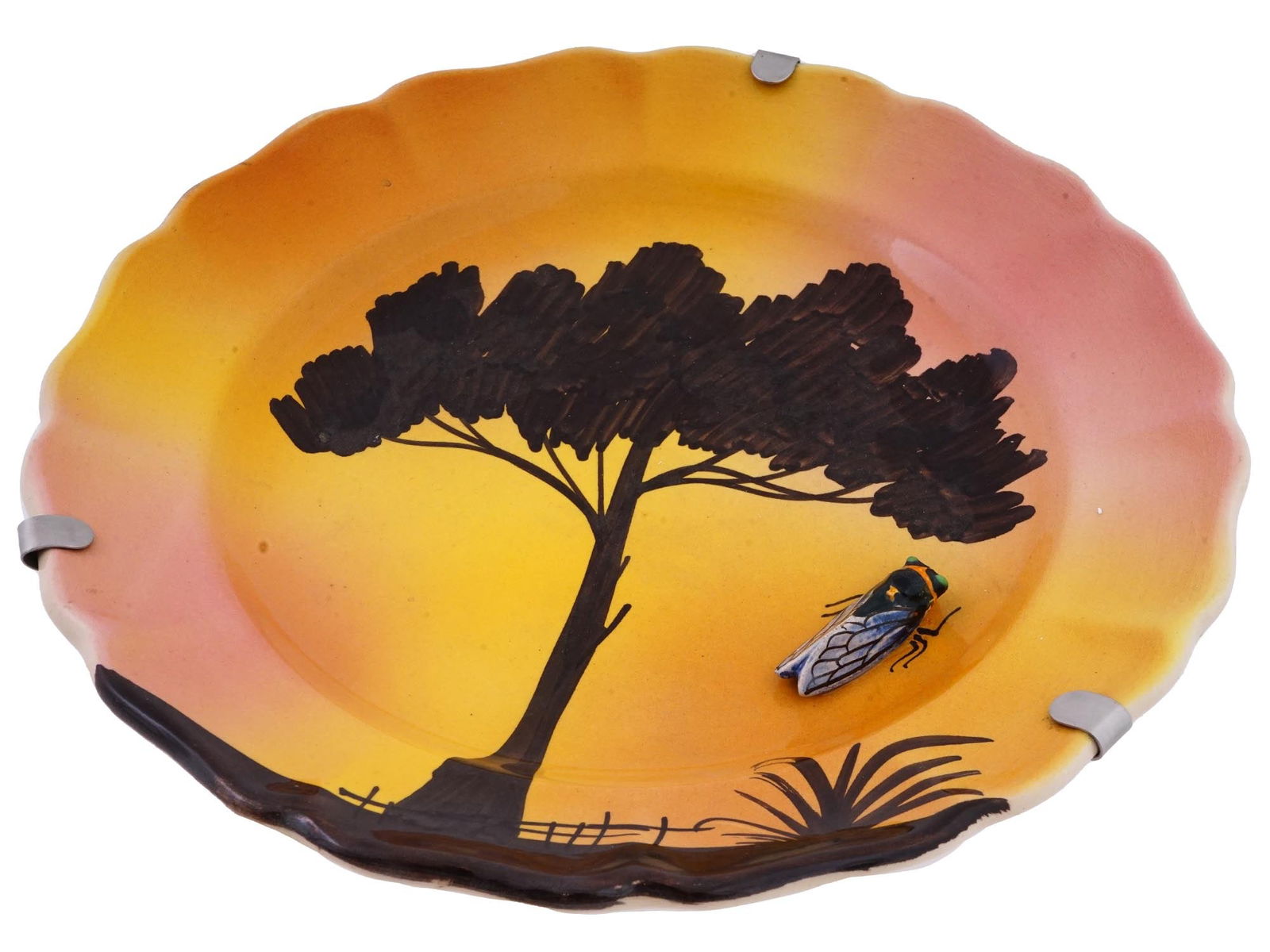 HANDMADE MID CENTURY FRENCH FAIENCE PLATE W CICADA: A handmade decorative faience plate with a relief cicada. This plate features a hand painted silhouetted landscape with a tall tree with a wide crown against the backdrop of a colorful pink orange sun