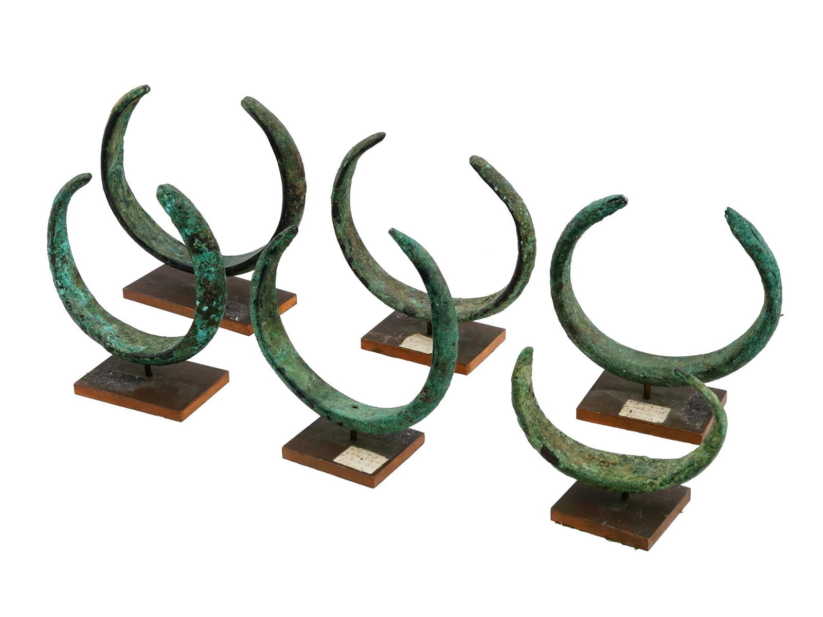 PERSIAN LORISTAN BRONZE CUFF BRACELETS W STANDS: A group of six ancient Luristan Persian bronze cuff bracelets, dating back to the 8th or 7th century BC. Each is mounted on a rectangular shaped wooden stand. Luristan bronzes are small cast objects d