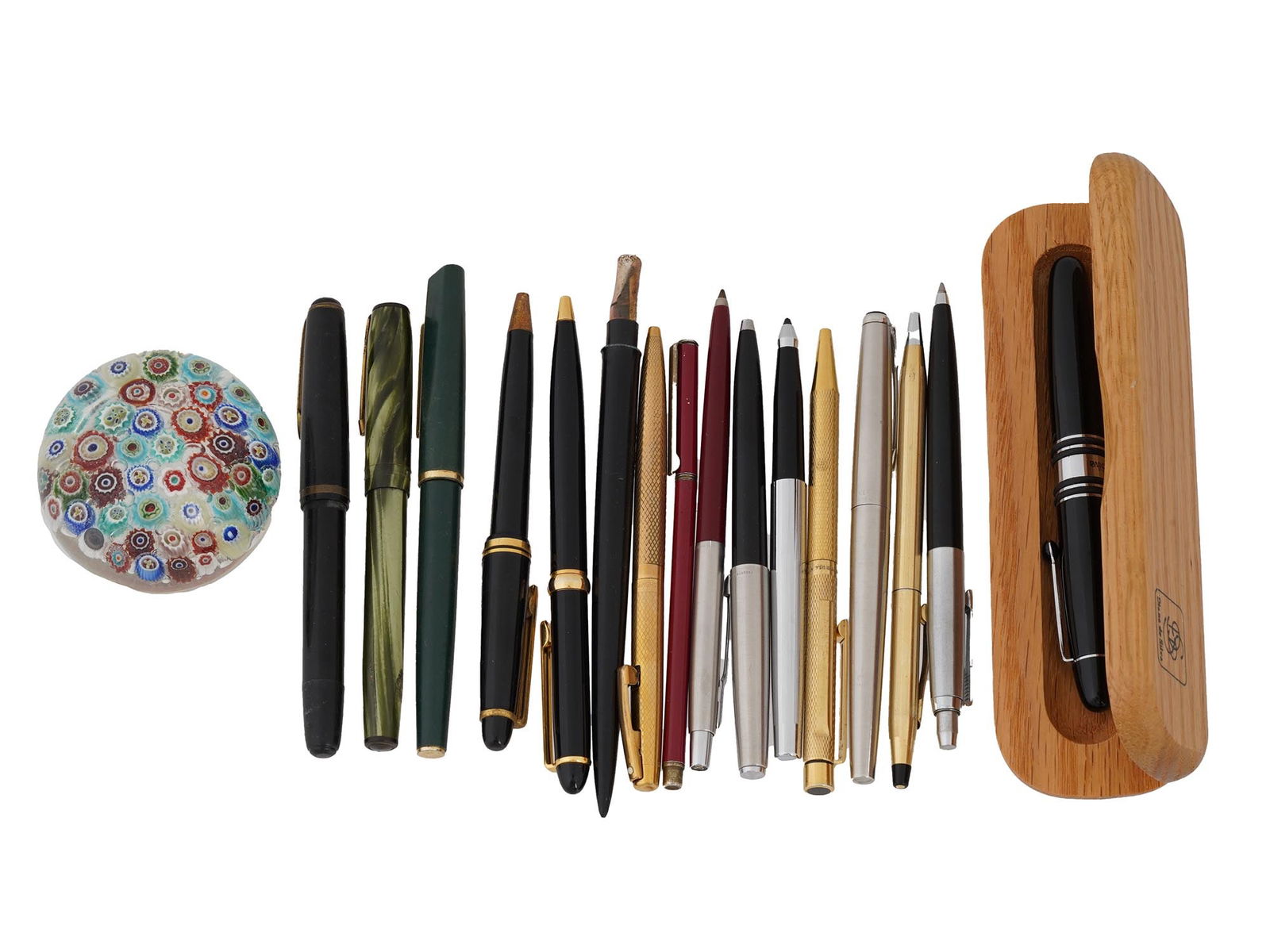 COLLECTION OF PENS WITH MILLEFIORI GLASS PAPERWEIGHT: A collection of pens with a paperweight. The pens vary in color and style, including black, green, gold, and silver tone, and some appear to be fountain pens while others are ballpoint pens. The paper