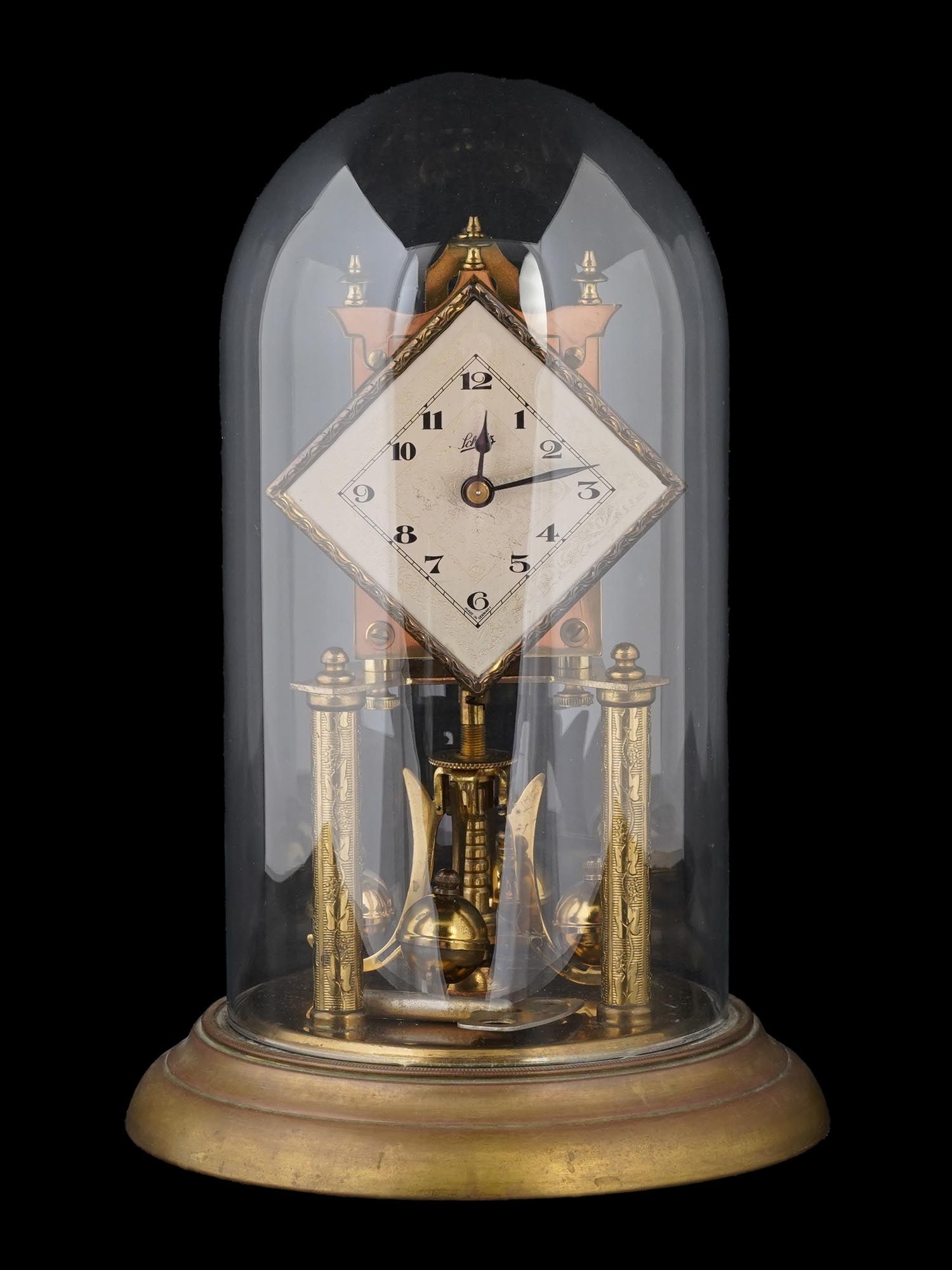WEST GERMAN TORSION PENDULUM CLOCK IN GLASS DOME: A West German gilt brass torsion pendulum clock, or anniversary clock by Schatz. Ca. 1950s. The mechanism represents a wheel with four chrome balls on ornate spokes, topped by the round clock face. Wh
