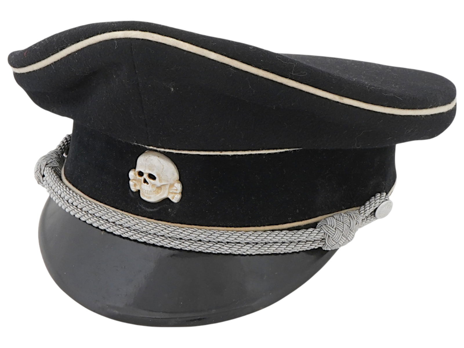 WWII NAZI GERMAN SS OFFICERS PEAKED VISOR CAP: A WWII Nazi German SS officers peaked visor cap made of black wool and leather. Skull with bones and a silver cord decorate the front. The Schutzstaffel, or SS was a major paramilitary organization un