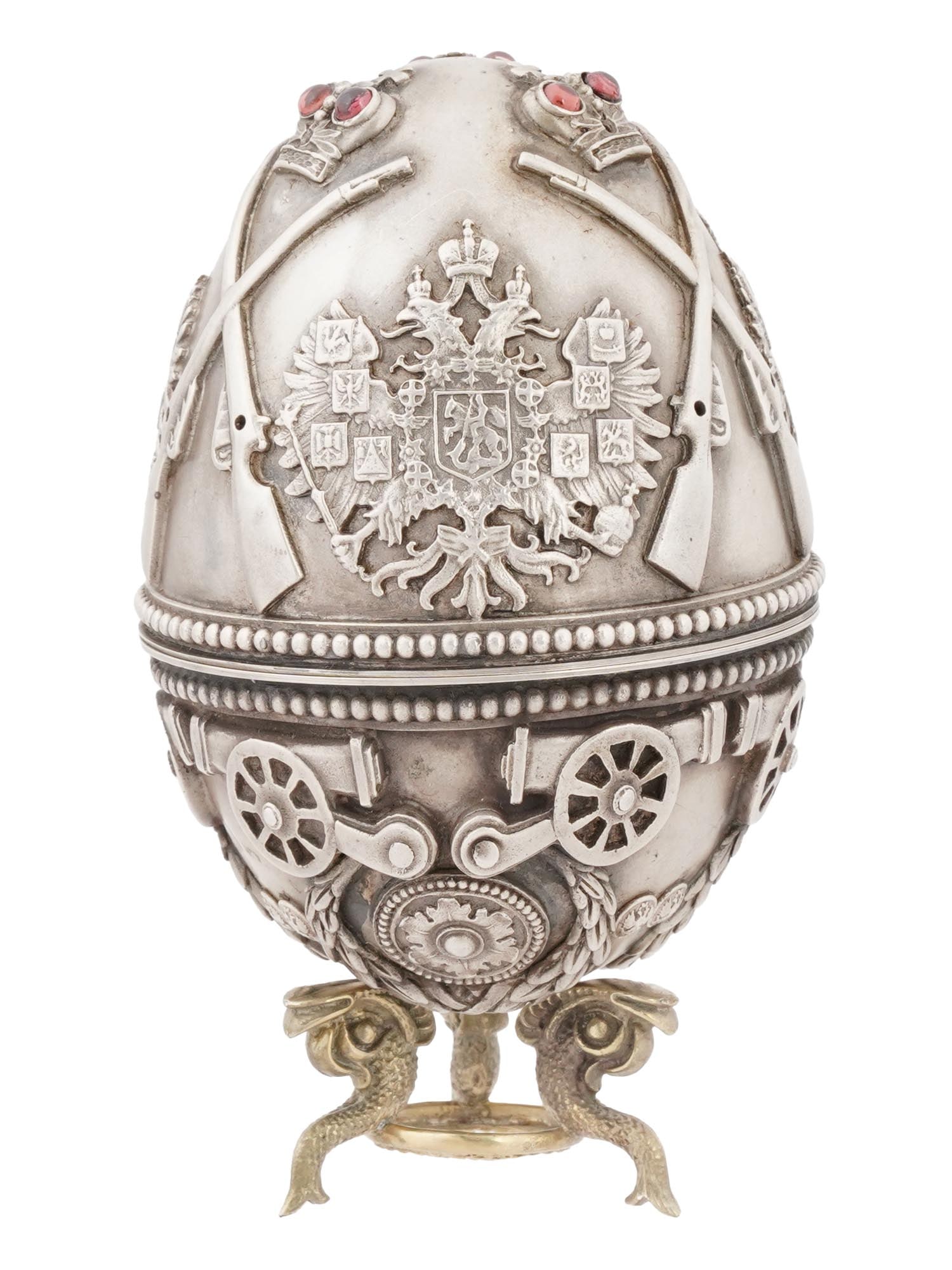 RUSSIAN MILITARY SILVER GEMSTONE EASTER EGG W STAND: A large Russian silver Easter egg with screw-on lid. The surface is embellished with relief Imperial Eagle coat of arms, crowns, rifles, and cannons. Gemstone cabochons embellish the crowns. The piece