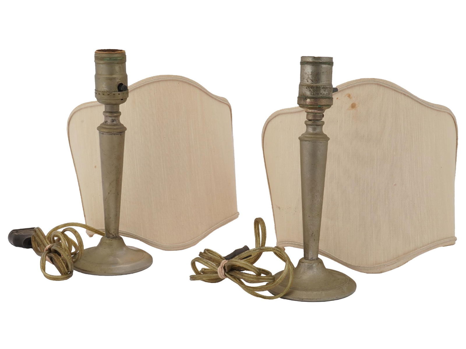 PAIR OF ANTIQUE BRYANT TABLE LAMPS WITH SHADES: A pair of identical antique early 20th-century American electrical table lamps. The brass lamps have a single light socket and half-round beige lamp shades. Hallmark Bryant 250 V Pat. Nov. 26 1907 is
