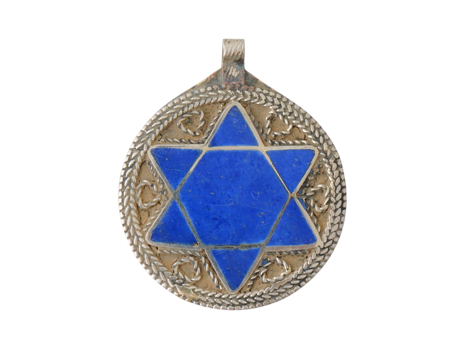 JUDAICA LAPIS LAZULI SILVER STAR OF DAVID PENDANT: An antique Judaica Star of David pendant set with a carved lapis lazuli stone into a silver setting. Circa 19th century. The Magen David is decorated with an applied braided pattern along the contour 