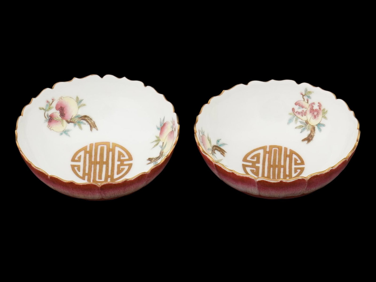 ANTIQUE CHINESE QING ERA FAMILLE ROSE PORCELAIN BOWLS: A pair of antique Chinese Famille Rose porcelain bowls, each featuring a scalloped rim and hand-painted floral and peach motifs symbolizing longevity and prosperity. The exterior is finished in pink o