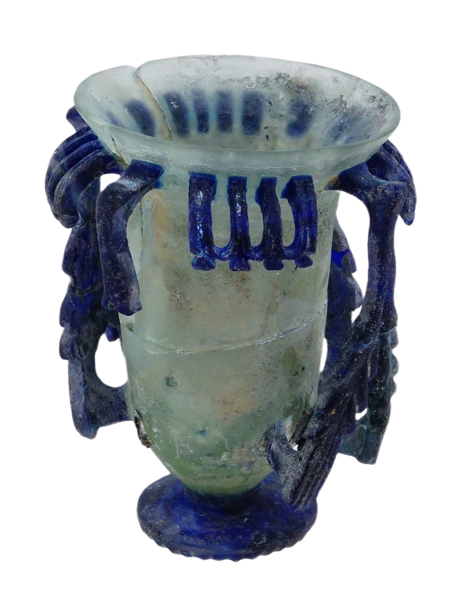 ANCIENT ROMAN CUT GLASS CANTHARUS GOBLET CUP: An ancient Roman cut glass footed cantharus goblet. The tall cylindrical goblet cup, widening towards the top, made of translucent glass, with cobalt blue handles and decorative elements with foliate
