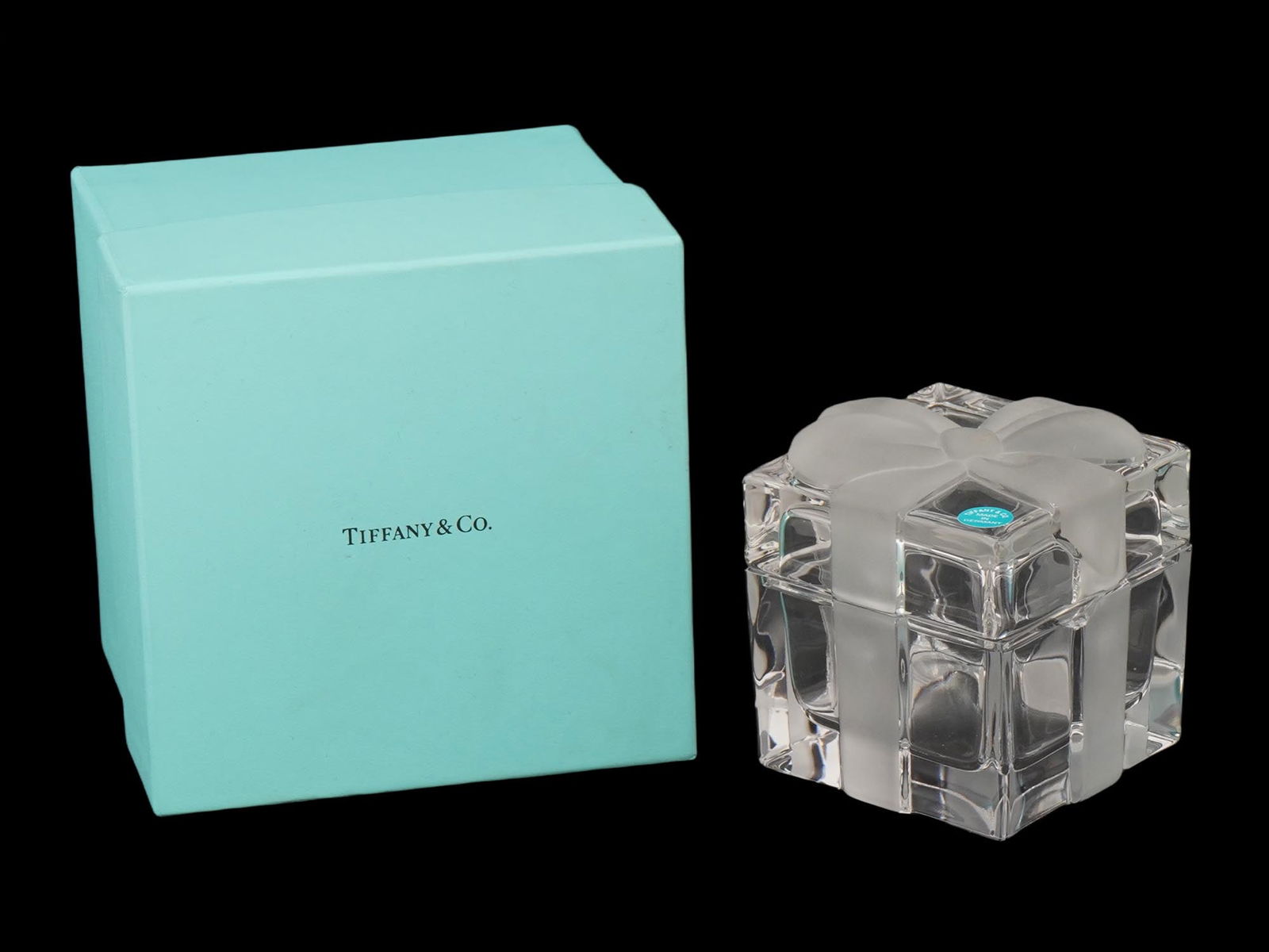 VINTAGE TIFFANY LIDDED CRYSTAL GLASS TRINKET BOX IOB: A vintage Tiffany and Co. crystal trinket box, usable as a paperweight or jewelry box, crafted from lead crystal glass. The square box features a clear body with a frosted ribbon and bow design on the