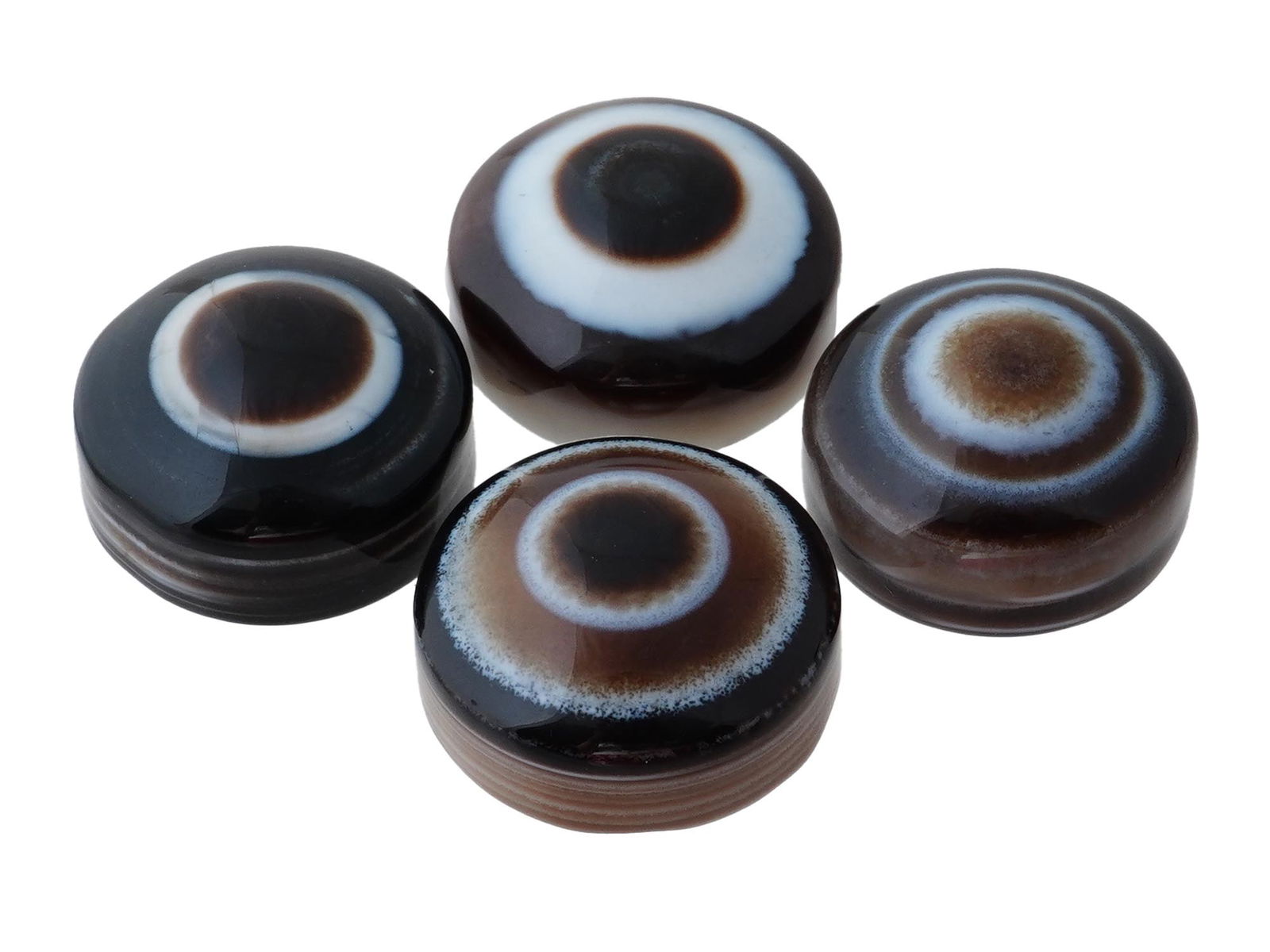 COLLECTION OF FOUR POLISHED EYE AGATE JEWELRY PENDANTS: A collection of four polished eye agate pendants, each hand-carved to enhance the natural concentric banding and eye formations characteristic of this gemstone. The stones display a range of earthy to