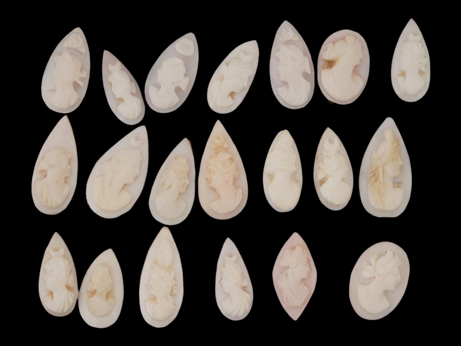 COLLECTION OF FEMALE PORTRAIT CARVED CORAL CAMEOS: A collection of hand carved pink coral cameos. A total of 20 items. Each piece depicts a female profile portrait rendered in high relief. Drop shape. Collectible Jewelry And Glyptic Art, Sculpture.