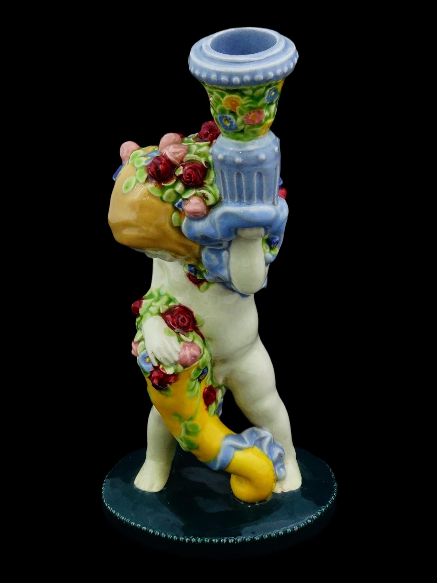 WIENER WERKSTATTE GLAZED CERAMIC CANDLE HOLDER: A glazed ceramic candlestick by Wiener Kunstkeramische Werkstatte, Vienna Art Pottery Workshops. Ca. 1920s. The piece is shaped as a putto with a cornucopia and flower vase. Embossed Werkstatte hallma