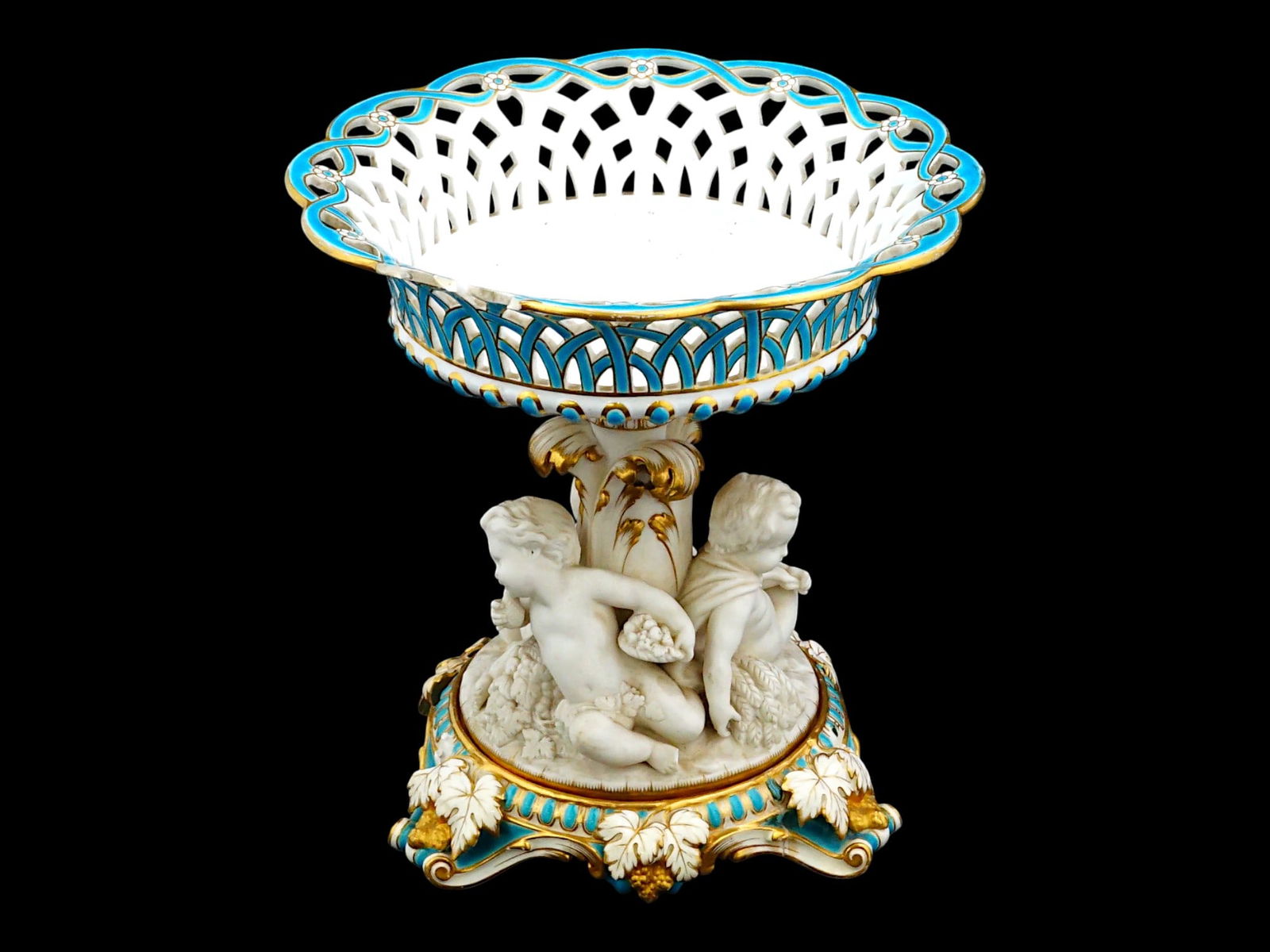 ANTIQUE MINTON BISCUIT PORCELAIN PUTTI CENTERPIECE: An antique 19th-century Minton biscuit porcelain figural centerpiece. It features a reticulated pierced bowl, glazed in a vibrant turquoise blue and white with extensive gilt highlights. The base is m