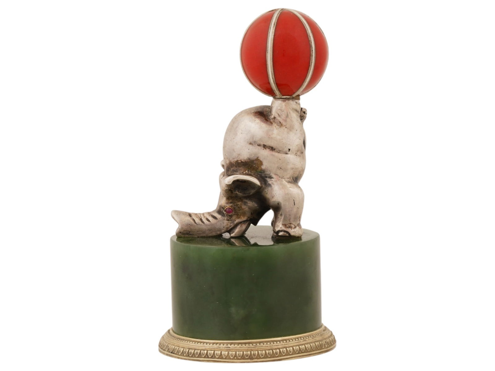 RUSSIAN SILVER ENAMEL JADE RUBY ELEPHANT FIGURINE: A Russian solid silver figure of a circus elephant holding a red and white enameled ball with his back feet. The eyes of the figurine are inlaid with ruby cabochons. The elephant is mounted on a