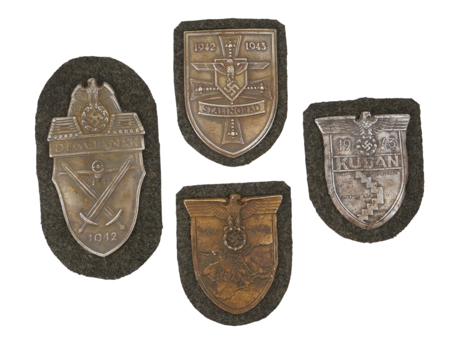 WWII TYPE GERMAN STALINGRAD CRIMEA KUBAN DEMYANSK SHIELDS: A group of four WWII type German military decorations, Stalingrad, Crimea, Kuban, and Demyansk shield badges. All four shield badges relate to military actions in the specified regions in 1942 and 194