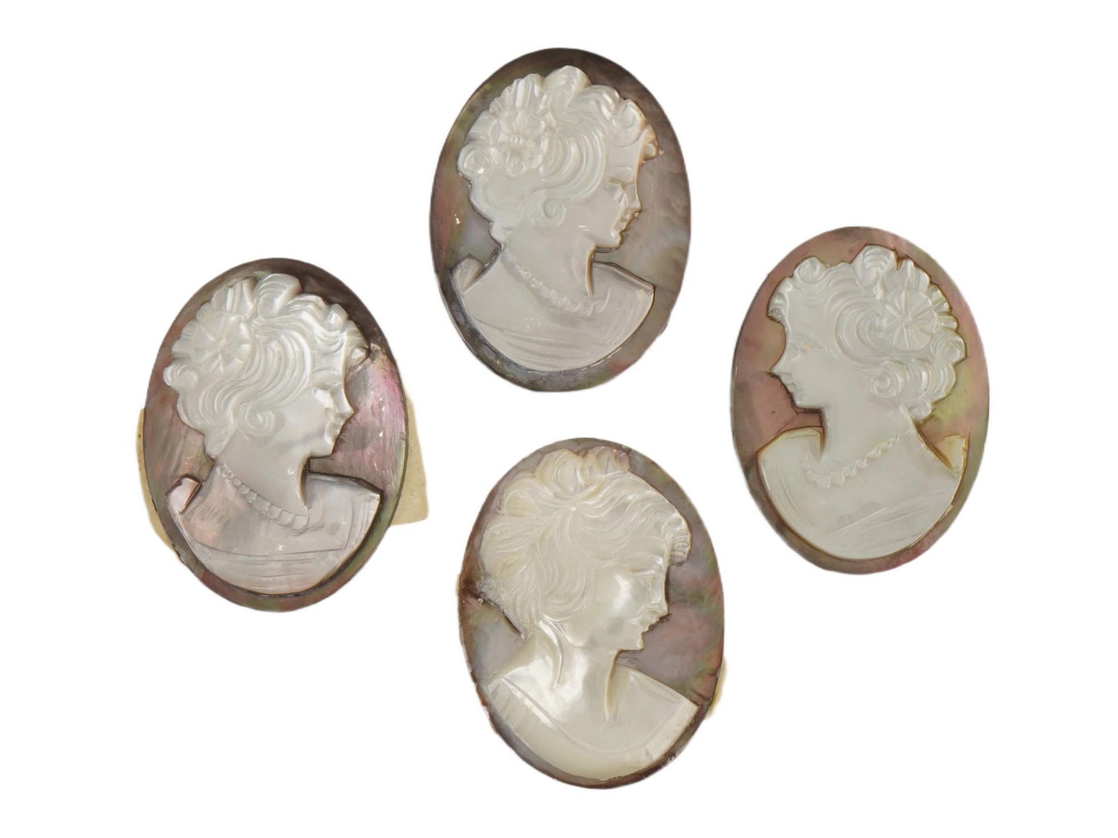 GROUP OF FOUR HAND CARVED SHELL PORTRAIT CAMEOS: A group of four shell cameos, each featuring a hand-carved female profile in relief utilizing the naturally contrasting layers of shell. Display a light cream or white foreground set against a darker,
