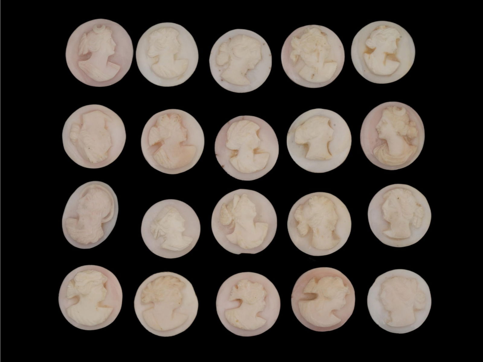 COLLECTION OF FEMALE PORTRAIT CARVED CORAL CAMEOS: A collection of hand carved pink coral cameos. A total of 20 items. Each piece depicts a female profile portrait rendered in high relief. Round shape. Collectible Jewelry And Glyptic Art, Sculpture.