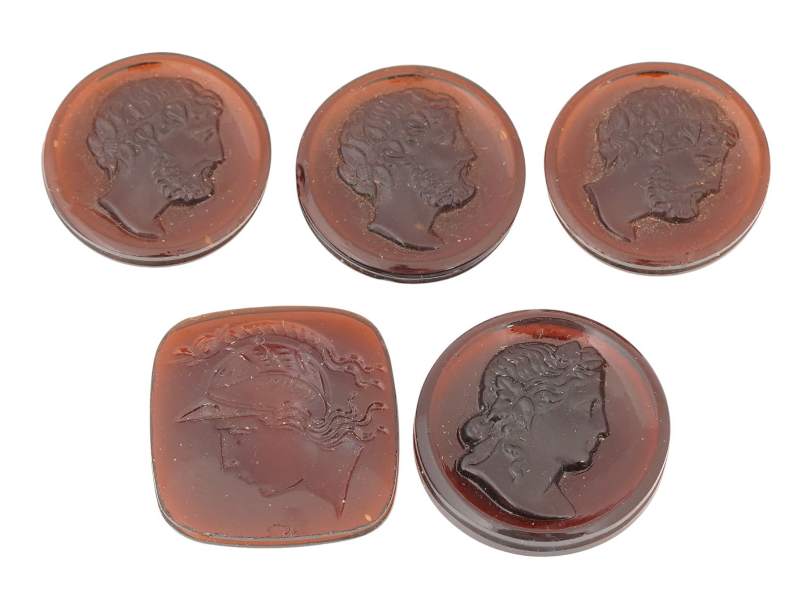 COLLECTION OF FIVE HAND CARVED CARNELIAN CAMEOS: A collection of hand carved carnelian cameos. A total of 5 items. Three cameos depict an identical male portrait in the right profile. Two cameos depict female portraits, including the helmeted goddes