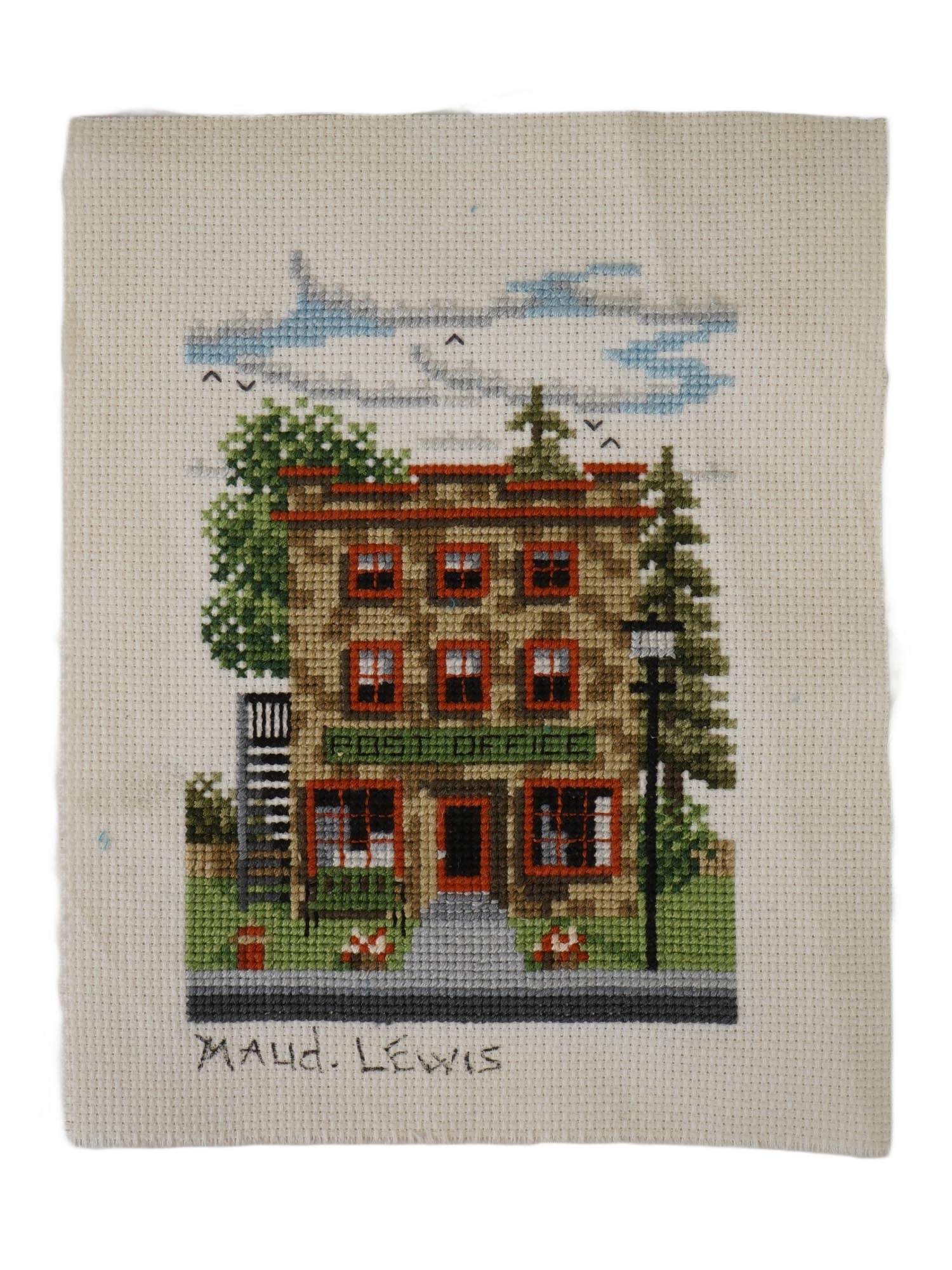CROSS STITCH NEEDLEPOINT SIGNED MAUD LEWIS: A finished cross-stitch needlepoint of a two-story post office building, signed Maud Lewis, lower left. Maud Lewis, Canadian, 1903 to 1970, was a Canadian folk artist from Nova Scotia. She lived most
