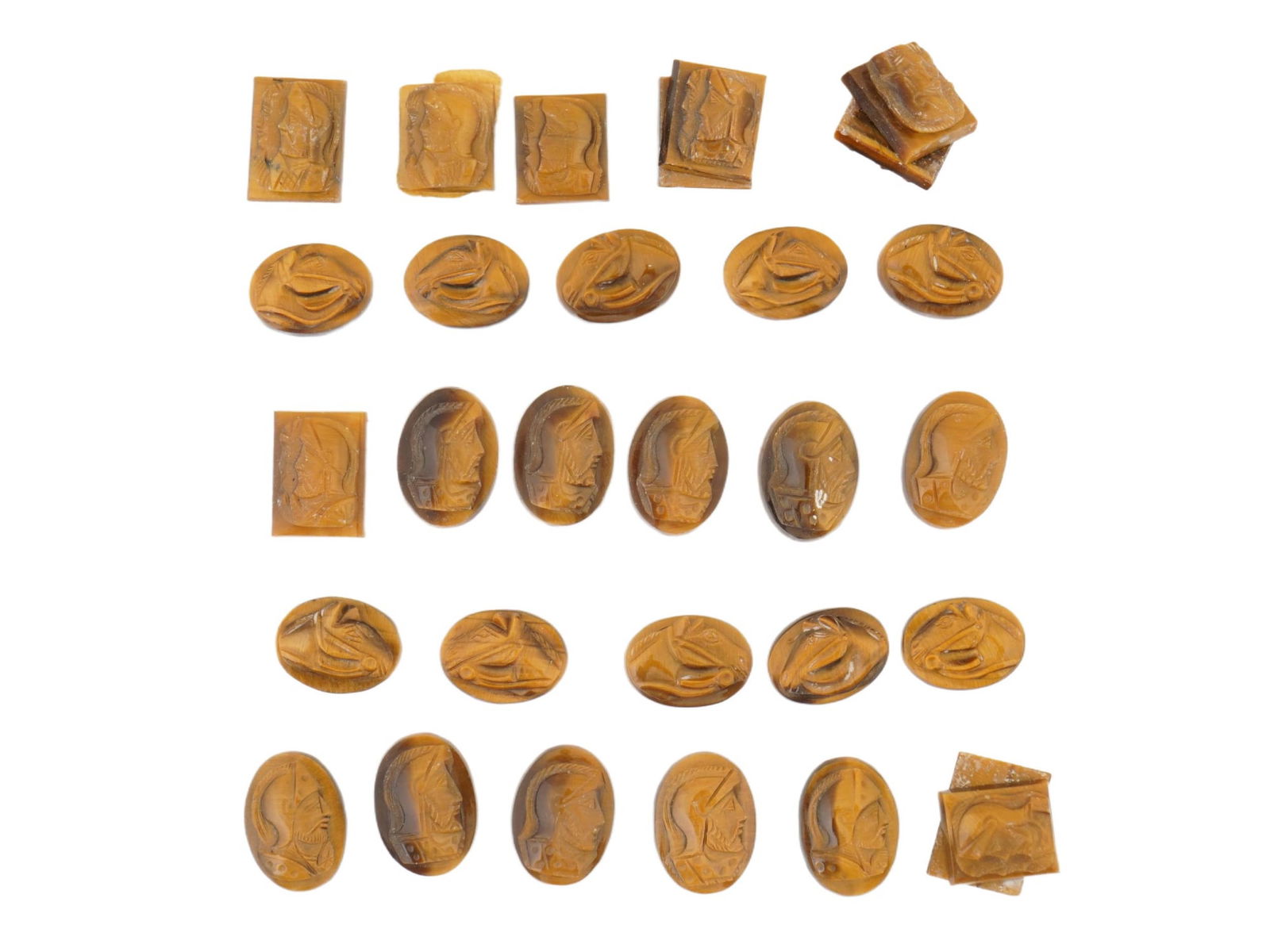 COLLECTION OF 30 CARVED NATURAL TIGERS EYE STONE CAMEOS: A collection of 30 hand carved natural tigers eye stone cameos. The cameos primarily depict a Roman or Greek soldiers profile bust, and some show a horses head. The cameos are formed as small rectangu