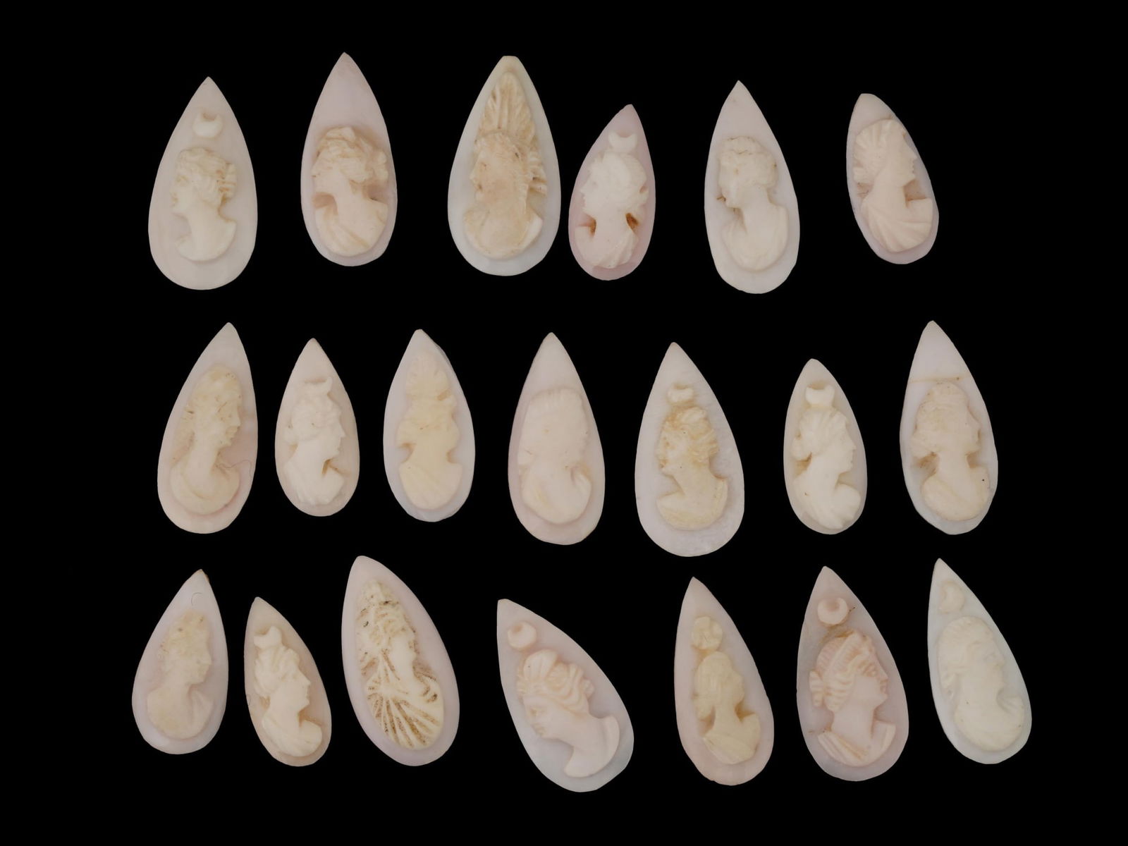 COLLECTION OF FEMALE PORTRAIT CARVED CORAL CAMEOS: A collection of hand carved pink coral cameos. A total of 19 items. Each piece depicts a female profile portrait rendered in high relief. Drop shape. Collectible Jewelry And Glyptic Art, Sculpture.