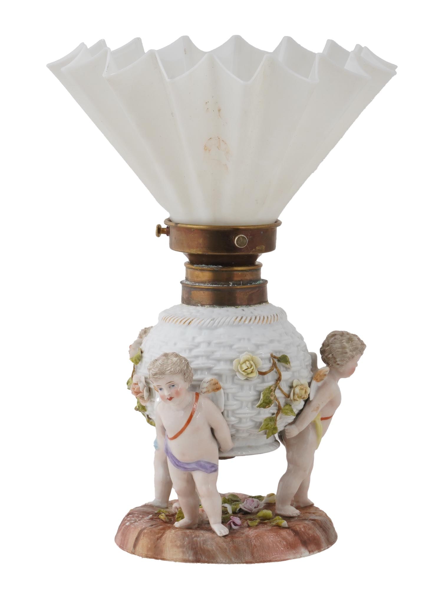 ANTIQUE GERMAN PORCELAIN W GLASS ELECTRIFIED LAMP: An antique German porcelain electrified lamp with milk white glass shade. The lamp in the shape of a round basket entwined with roses, held by a group of three sculpted winged cherubs. The lampshade h
