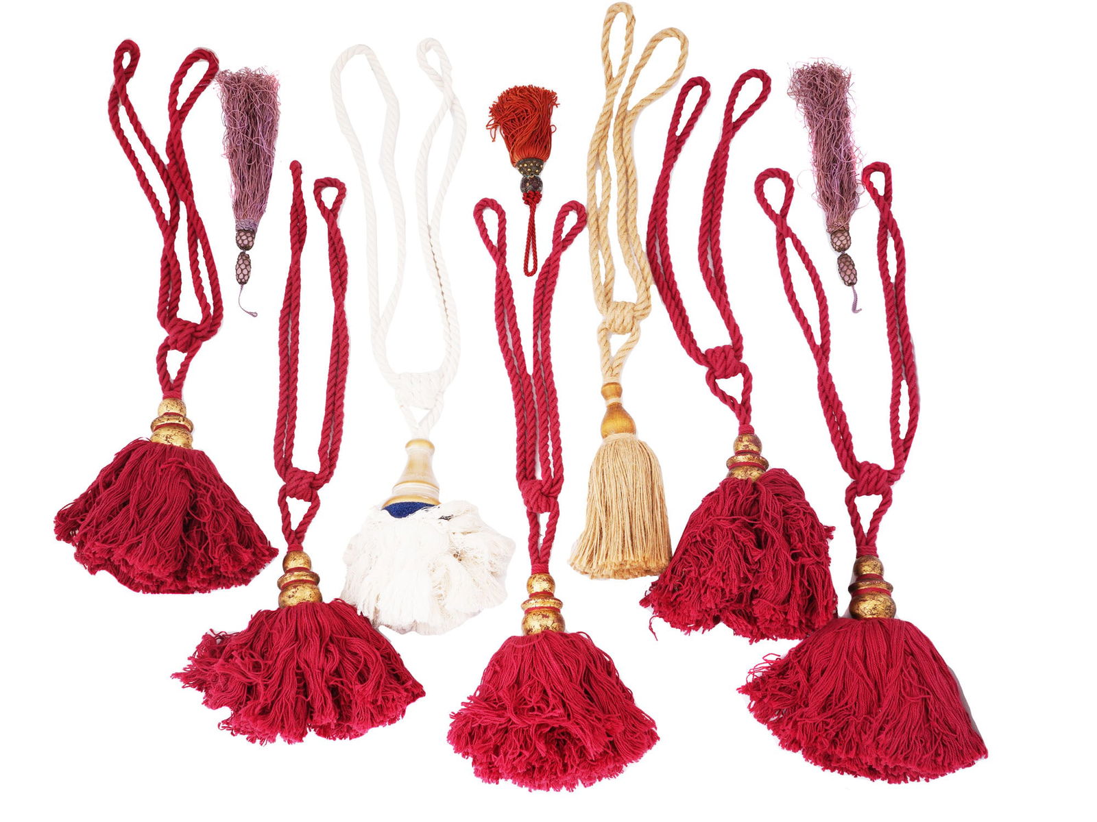 COLLECTION OF VARIOUS CURTAIN TASSELS: A collection of curtain tassels in a variety of colors and styles. Many of the tassels are red and feature a dense, fringed design with decorative metal and wooden elements at the top. There are also