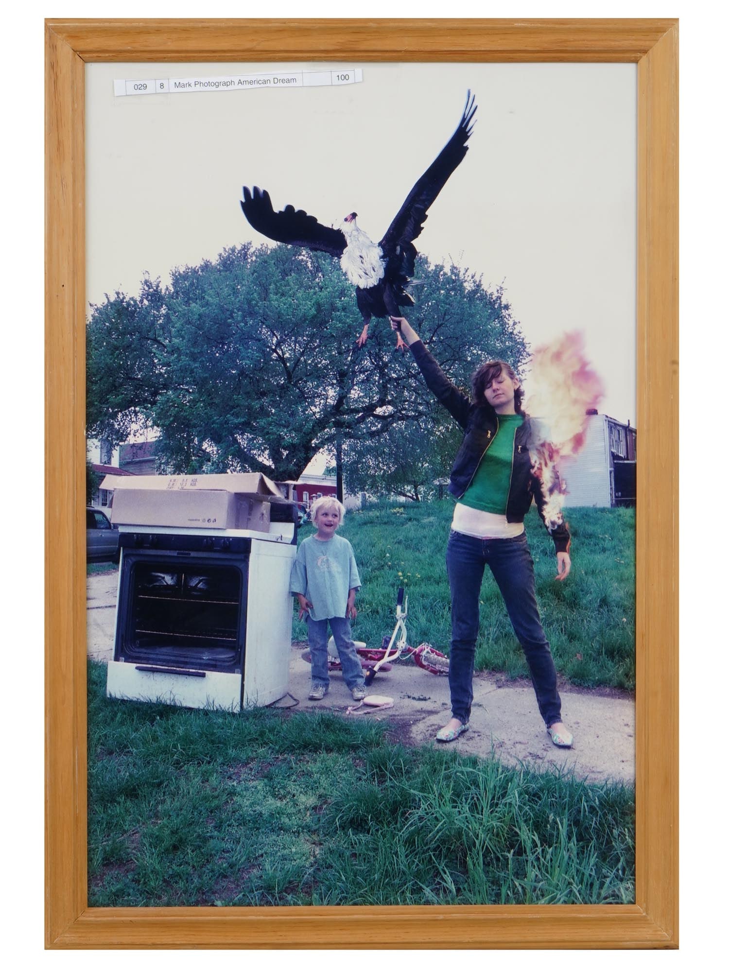 VINTAGE AMERICAN PHOTOGRAPH TITLED AMERICAN DREAM: A vintage American ironic photograph titled American Dream. The artwork depicts a young woman holding a flying eagle with one hand and another hand in fire. The photo is accompanied by a paper note