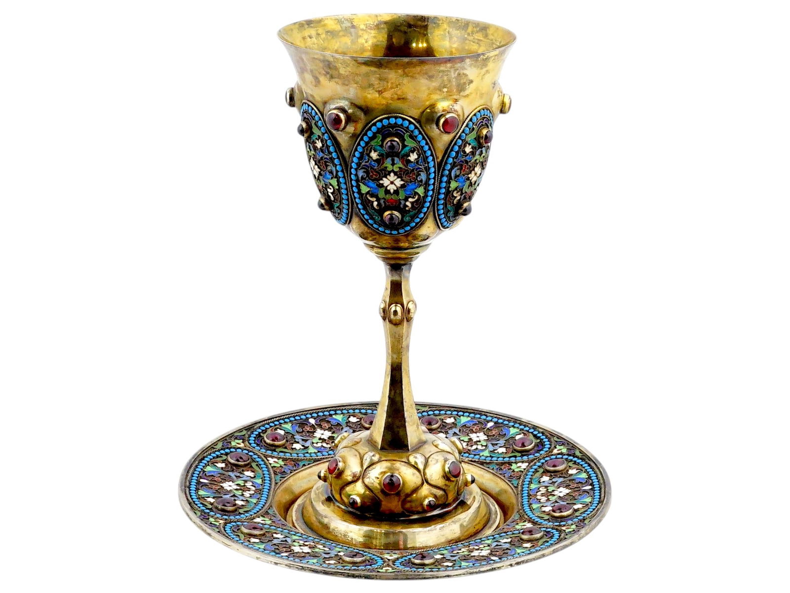 JUDAICA RUSSIAN 84 SILVER GARNET KIDDUSH CUP PLATE: A Judaica Russian 84 gilt Silver and enamel set of a Kiddush cup and a plate. The wares are adorned with oval shaped medallions, covered with polychrome floral, foliage, and geometrical patterns made