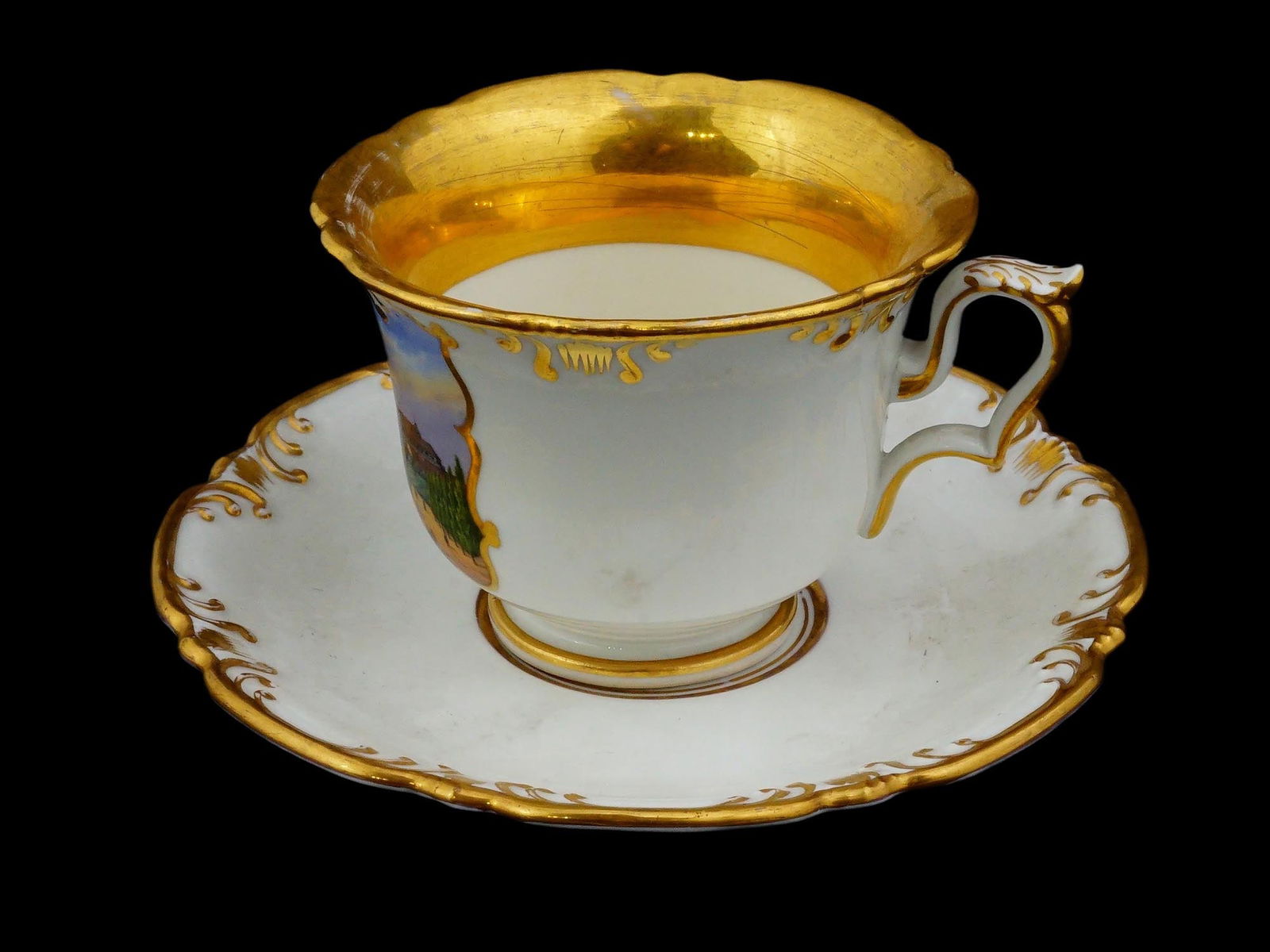 ANTIQUE GERMAN SPM PORCELAIN GILT VIEW CUP AND SAUCER: An antique porcelain gilt-finished view cup Ansichtentasse and matching saucer by Schumann Porzellan-Manufaktur, dating to the early 19th century, reflecting the Biedermeier-era fascination with