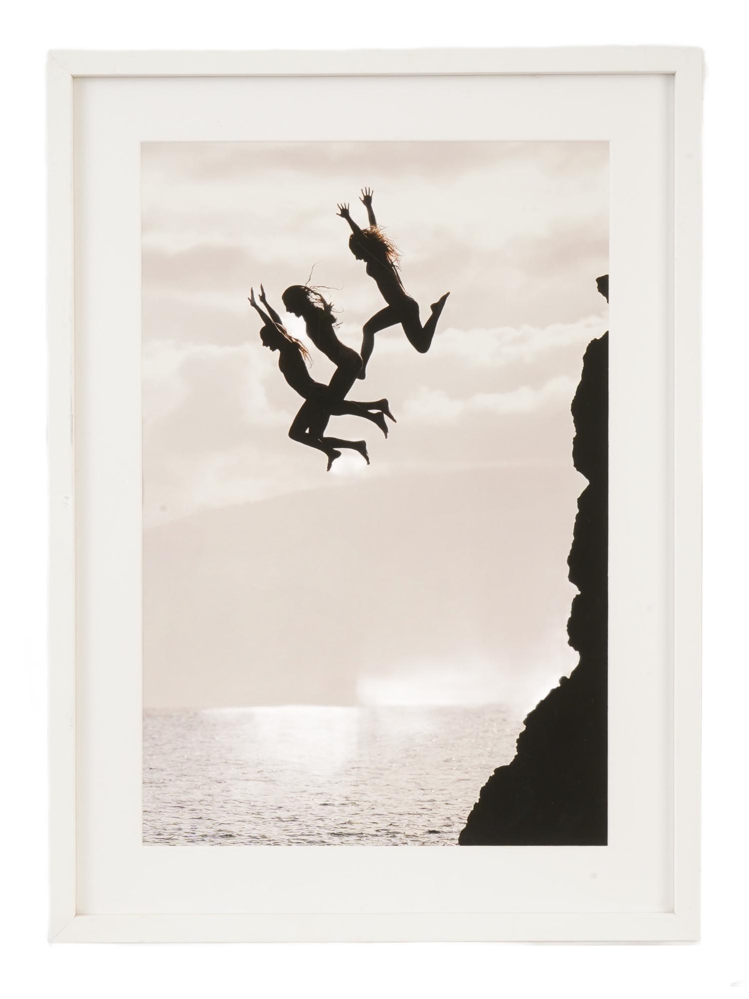 PHOTO PRINT THREE NUDE BY REBECCA AMBER AND LINDSEY SARA: A framed photo print, titled The Leap, is a collaborative work by photographers Rebecca Amber and Lindsey Sara of Nordic Retreats. The minimalist image captures the silhouette of three nude female fig