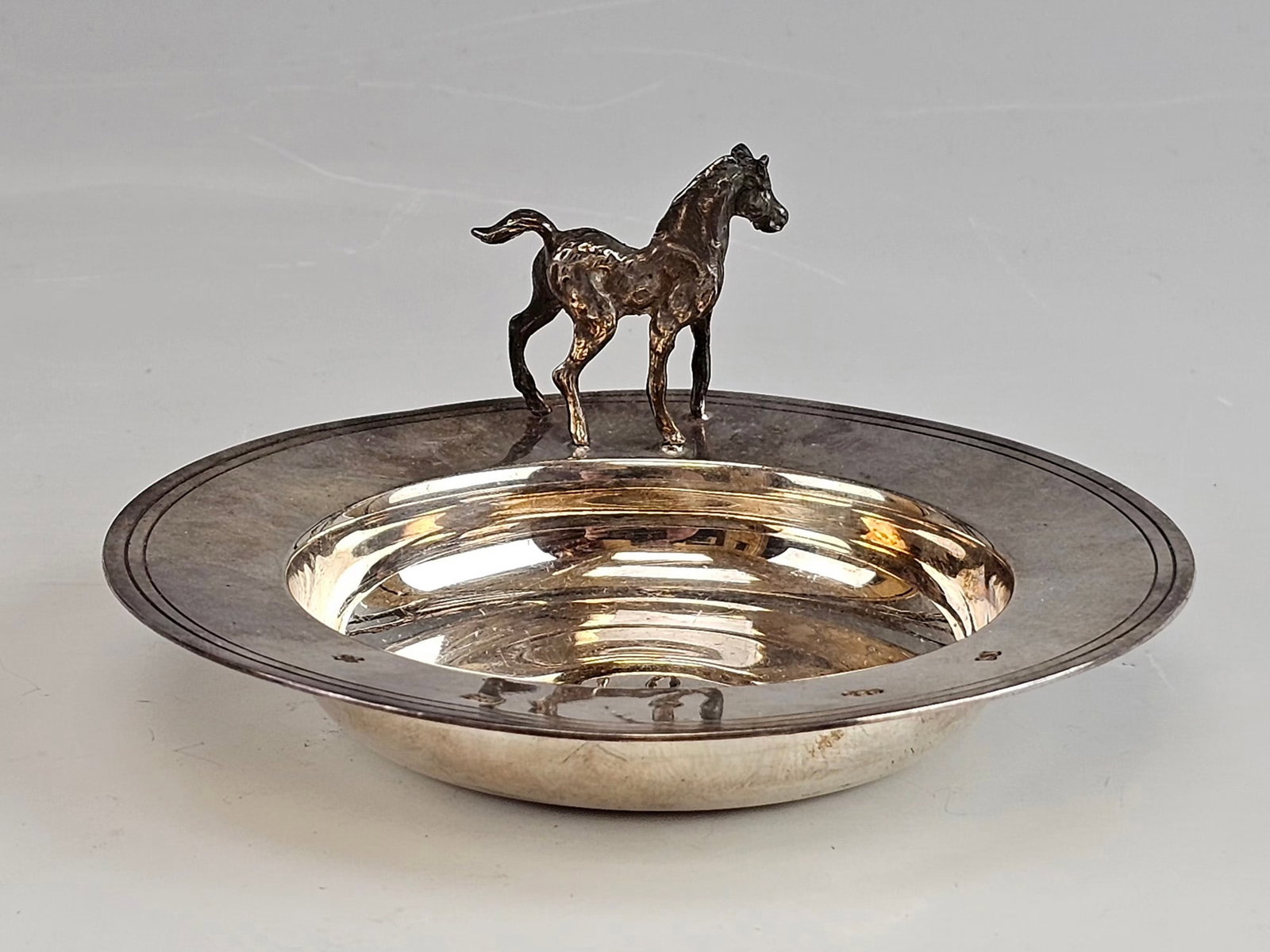 ANTIQUE EUROPEAN STERLING SILVER DISH W A HORSE FIGURE: An antique European sterling silver dish, featuring a modeled horse figure mounted at the edge of a shallow circular tray. Likely intended as an ashtray or trinket dish. Hallmarked. Dating to the
