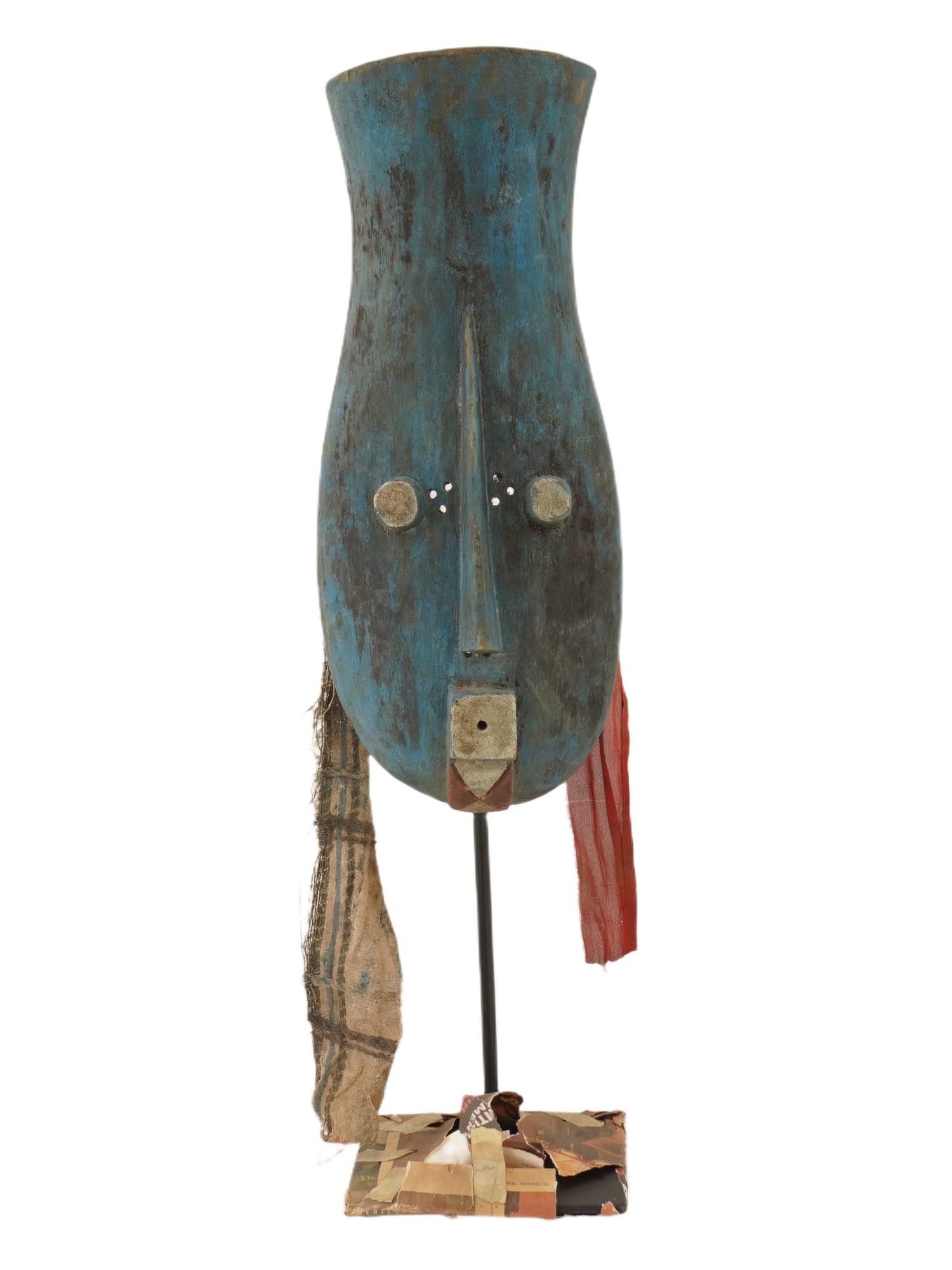 AFRICAN LIBERIAN GUERE PAINTED WOODEN MASK IVORY COAST: An African hand carved and blue painted wood hunting mask from the Guere tribe of Liberia. The Guere mask of an elongated form is decorated with fabrics. Mounted on a stand. Note: used by hunters to k
