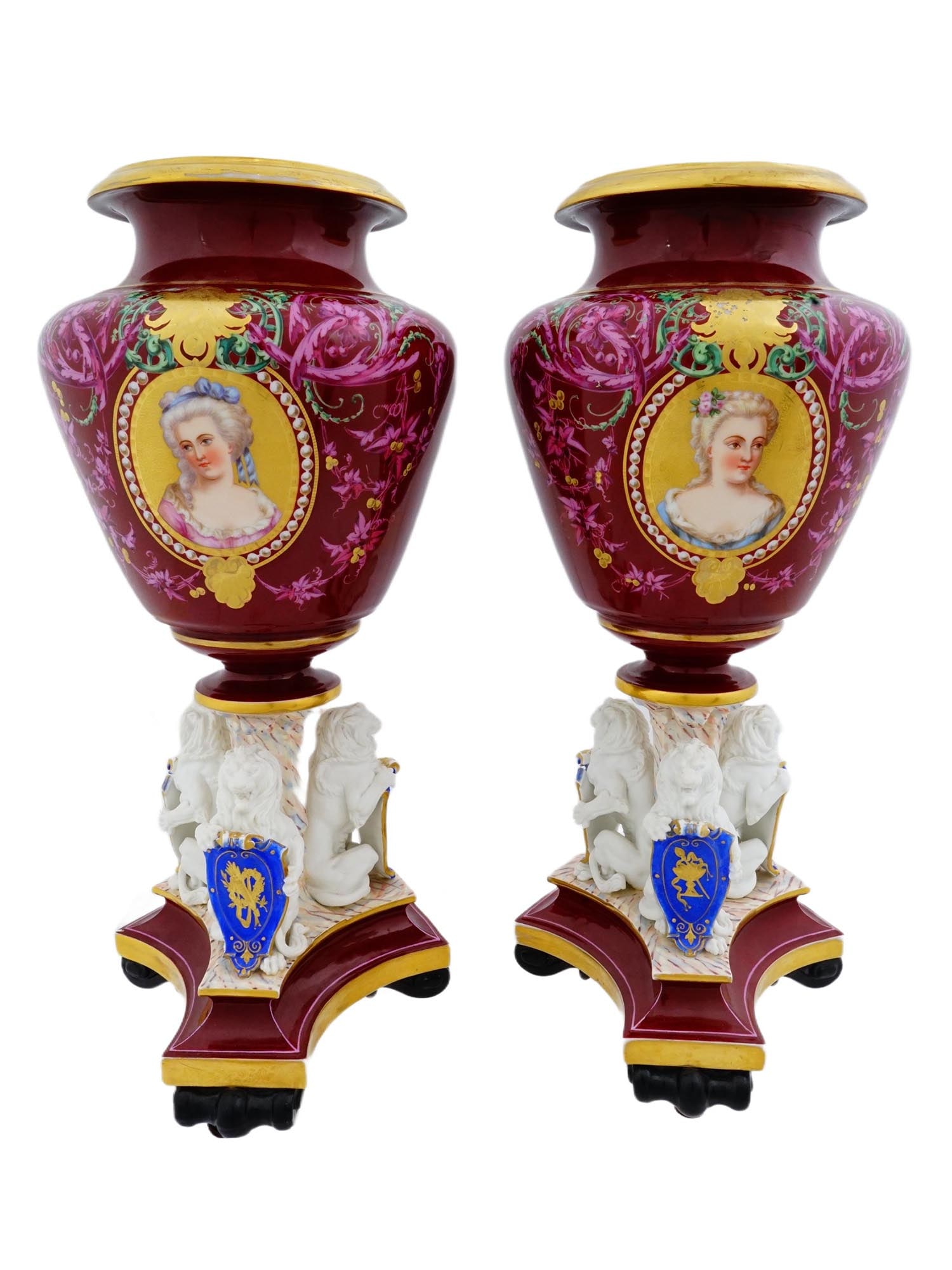 PAIR OF ANTIQUE 19TH C EUROPEAN PORCELAIN URN VASES: A pair of antique European porcelain urn vases in Louis XV manner. The urn vases are supported by architectural tripod pedestals and feature a burgundy background with gilded elements. Decorated with