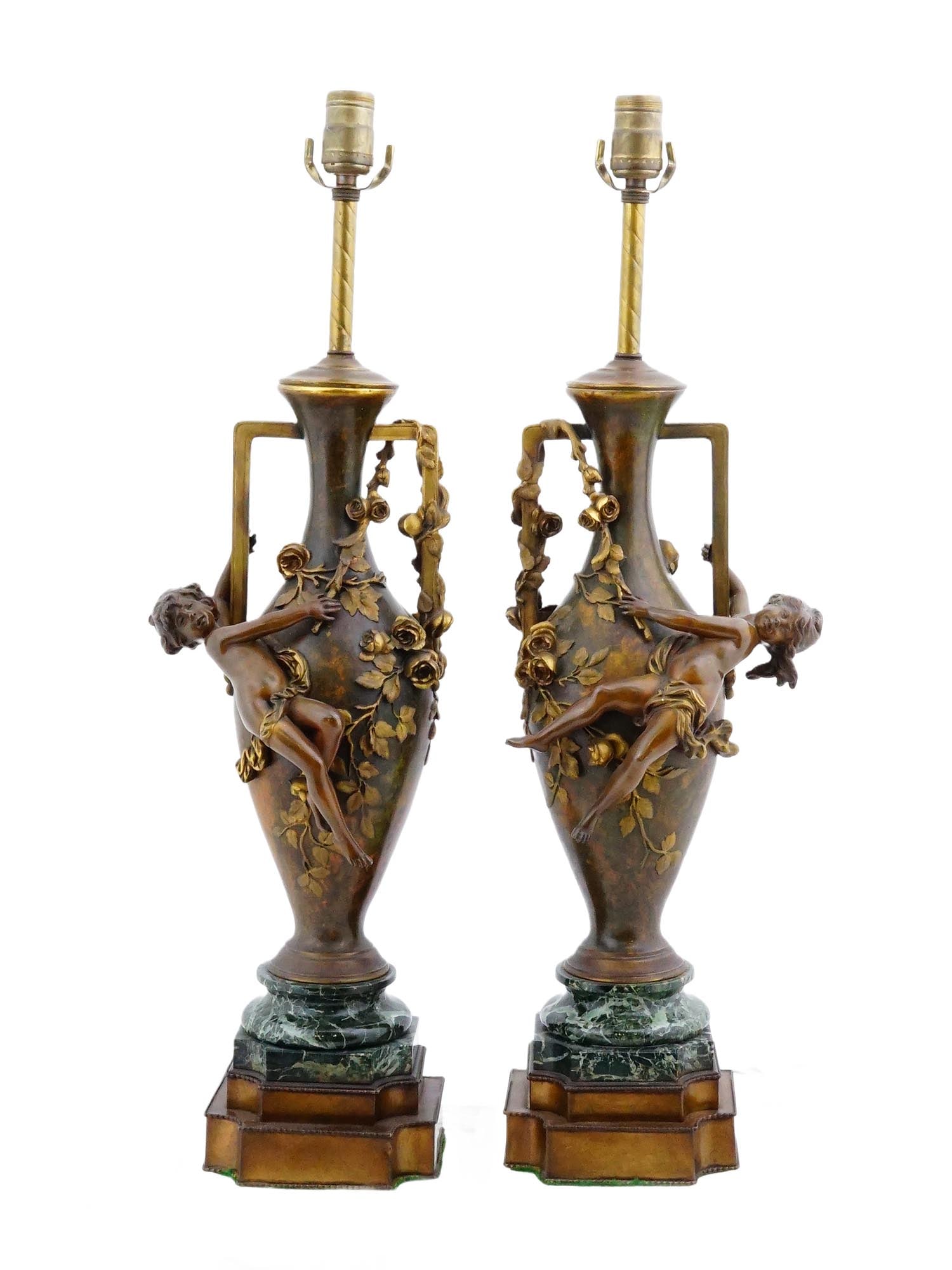 PAIR OF ANTIQUE FRENCH ART NOUVEAU TABLE LAMPS: A pair of antique French Art Nouveau table lamps. The lamps feature bronze urn-form bodies decorated with high-relief figures of climbing putti amidst floral garlands. Each lamp is flanked by minimali