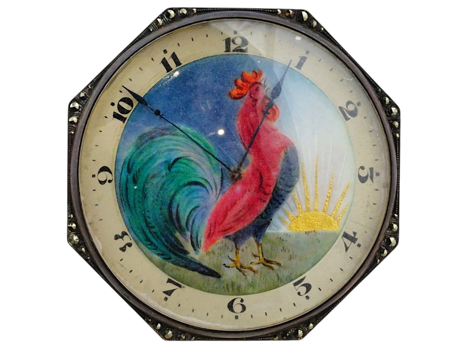 ART DECO DESK ENAMEL CLOCK WITH ROOSTER: An Art Deco desk clock features an octagonal metal frame surrounding a polychrome enamel dial that depicts a vibrant rooster against a stylized sunrise and starry sky background. The dial is set with