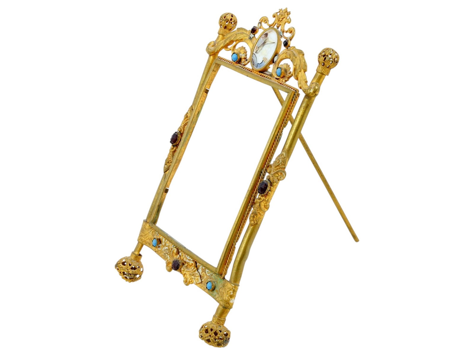 EUROPEAN JEWELED GILT BRASS EASEL PICTURE FRAME: A decorative easel back picture frame. The ware is constructed from brass with a weathered gilt finish, exhibiting a Neoclassical architectural form characterized by fluted side columns and scrolled f